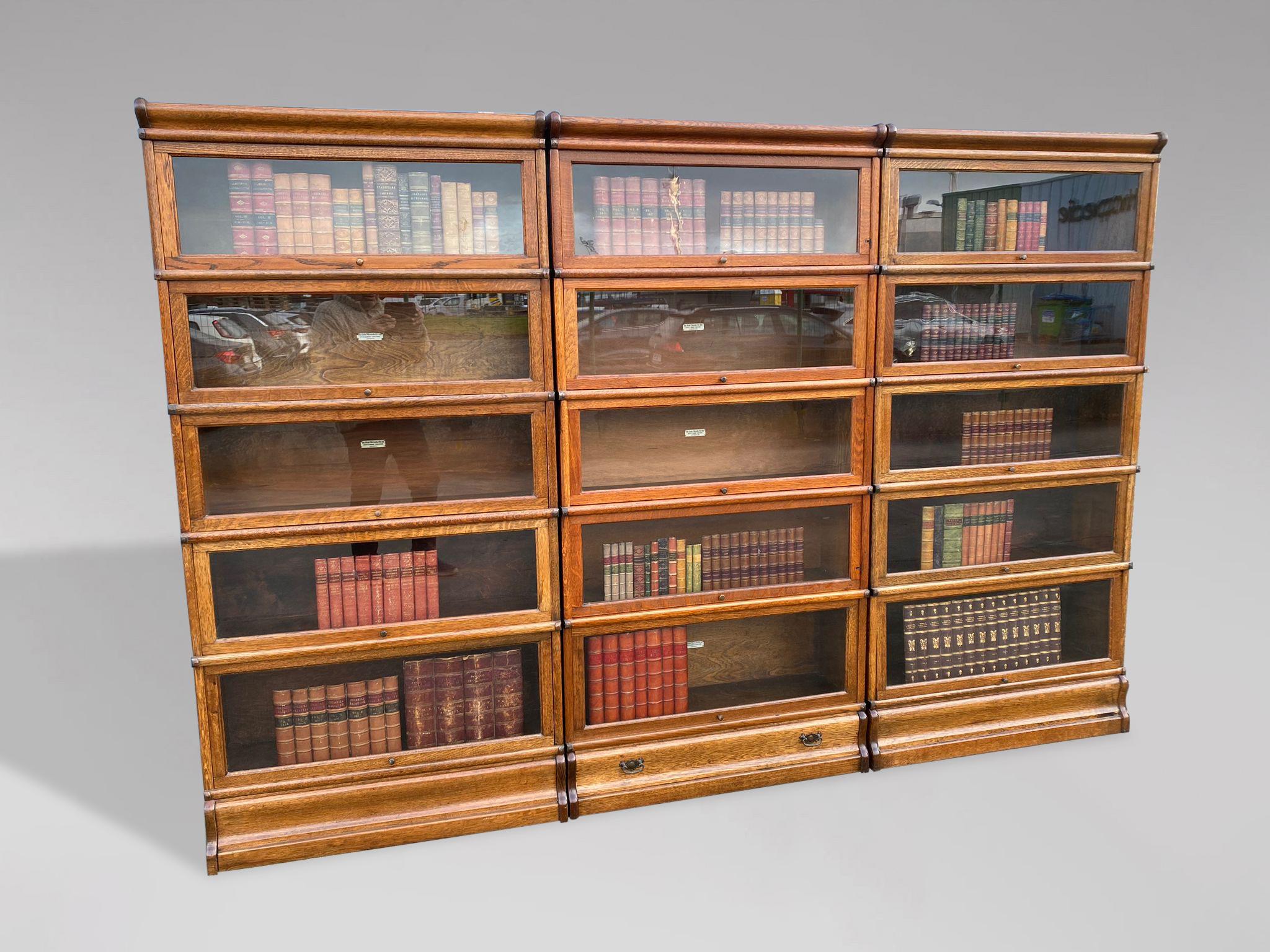 A large set of 3 solid oak antique Globe Wernicke 7 section bookcases. Moulded cornice top above 5 glazed sections with original glass doors, original mechanism and original brass knob handles, standing on a moulded plinth and copper strapping to