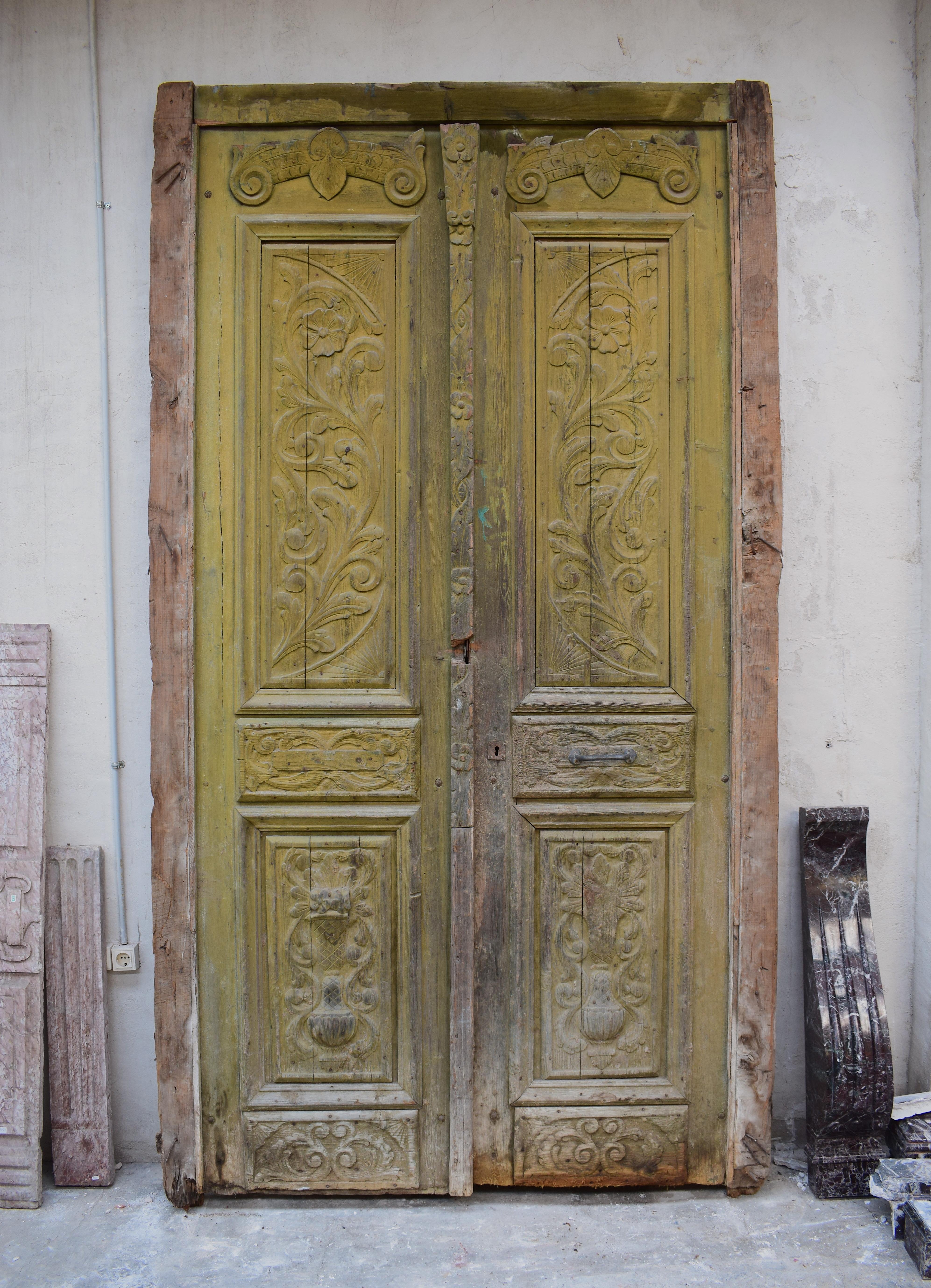 This set of large antique exterior doors have great hand crafted raw detail carved into each panel. They are from an old house and are architectural salvage. The doors have a beautiful green and yellow patina colour across their surfaces. Each door