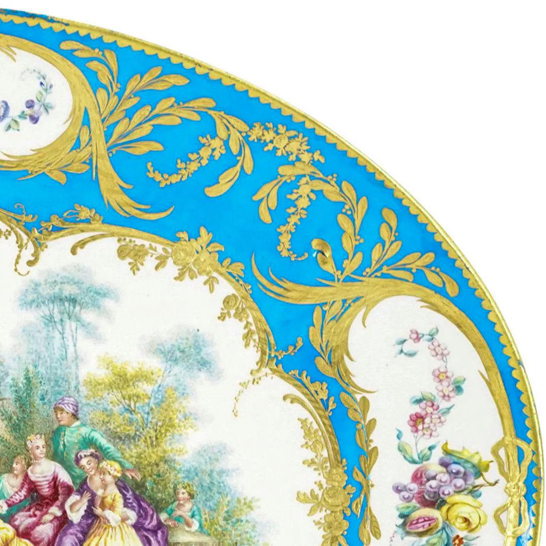 Our lovely porcelain charger in the Louis XV style from the late 19th century is distinguished by its large size, 18 3/4 inches (47.6 cm) across.

It depicts members of the court engaged in a blindfold game with bleu celeste (turquoise) glaze with