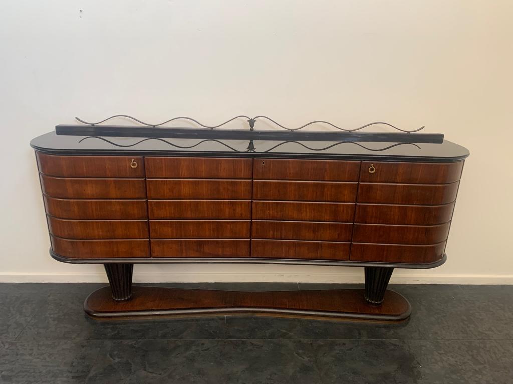 Sideboard attributed to Vittorio Dassi. 
The elegantly ovalised base narrows towards the centre. Profiled and outlined above by ebonizing, below by brass plate. 
The base accommodates two vase-shaped columns carved in a thousand rows and ebonised,