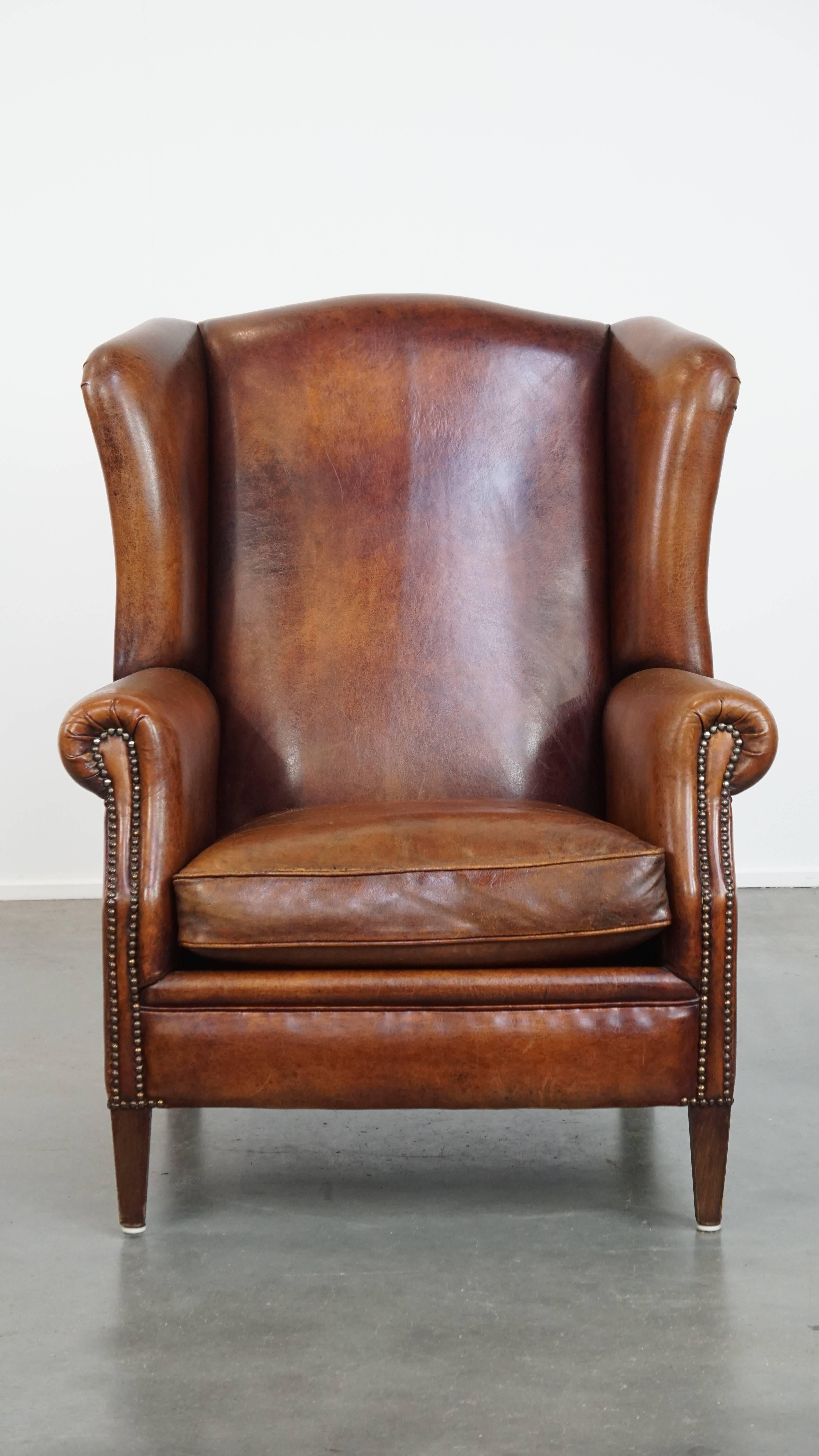 Offered here is this large, generous sheepskin wingback armchair with warm tones and a beautiful patina. 

Crafted from sheepskin leather, this armchair exudes elegance through its shape, warm color palette, and refined details such as decorative
