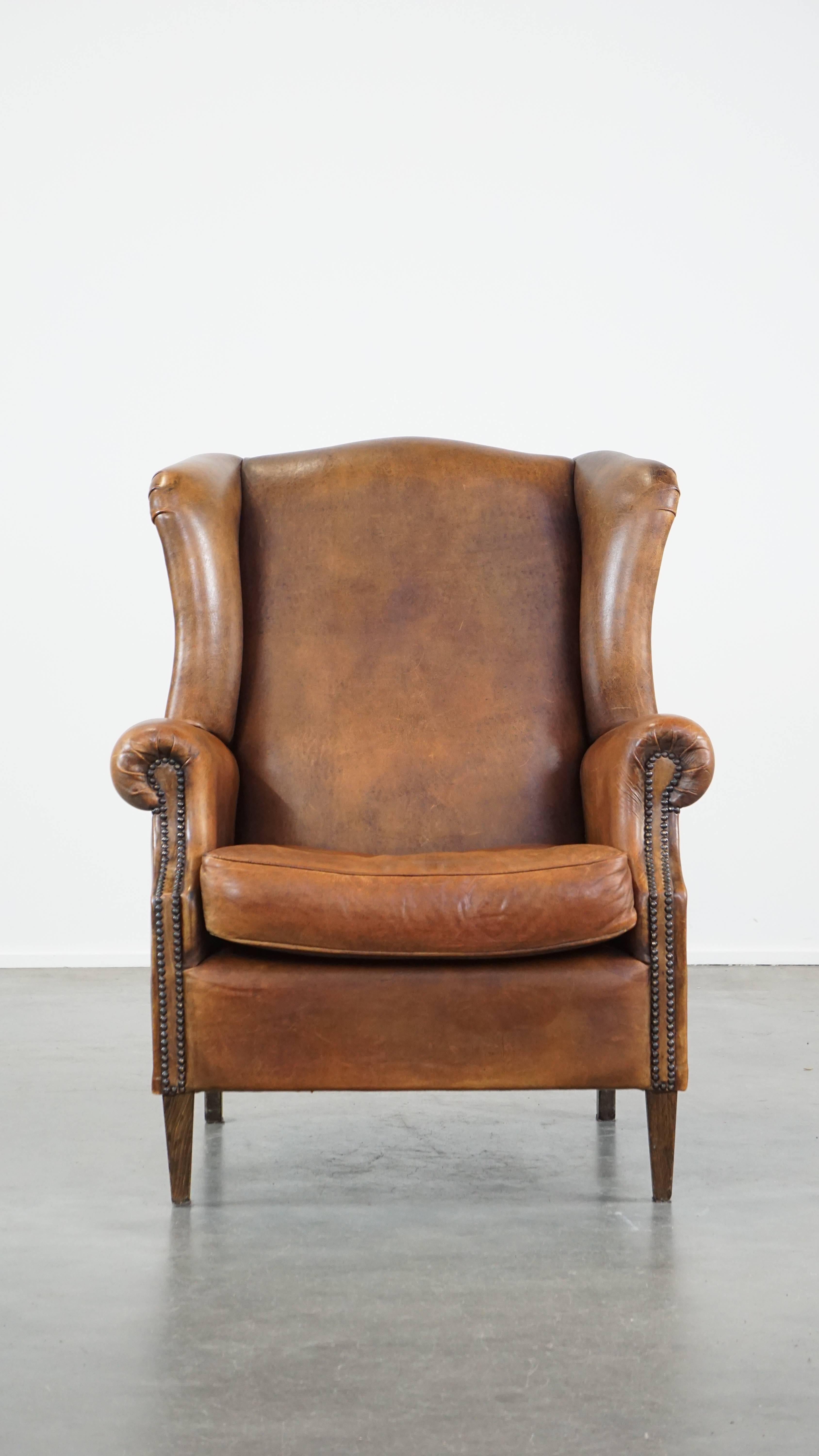 Este gran sillón orejero de piel de oveja es la combinación definitiva de encanto y comodidad. Es el lugar perfecto para relajarse tras un largo día. Este sillón con respaldo alado presenta bellos colores y está acabado con clavos decorativos. Viene