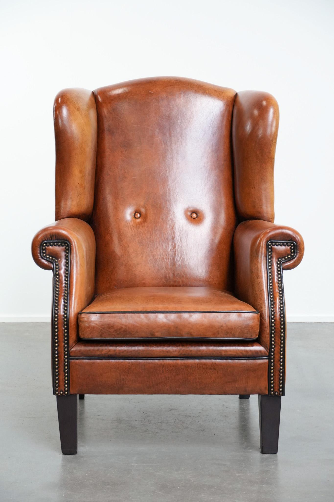 Ce magnifique fauteuil à oreilles en peau de mouton, de grande taille, est un ajout élégant et confortable à tout intérieur. La finition raffinée avec des passepoils noirs et des clous décoratifs confère au fauteuil un aspect classique, luxueux et