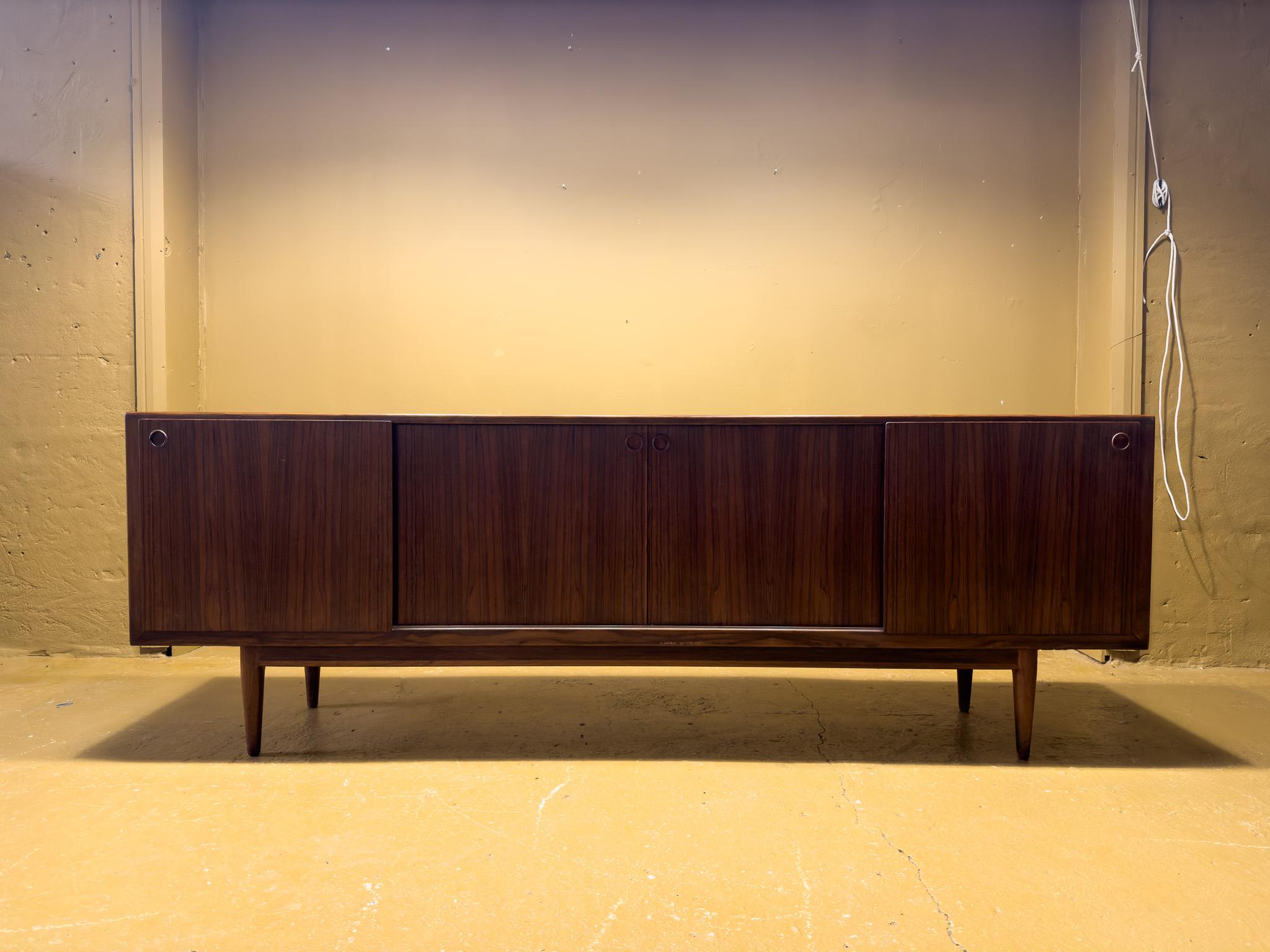 This stunning 1960s Danish mid-century sideboard showcases exquisite craftsmanship and rich wood grain detailing, combining sleek aesthetics with exceptional functionality. The design is defined by clean lines, subtly recessed handles, and elegant