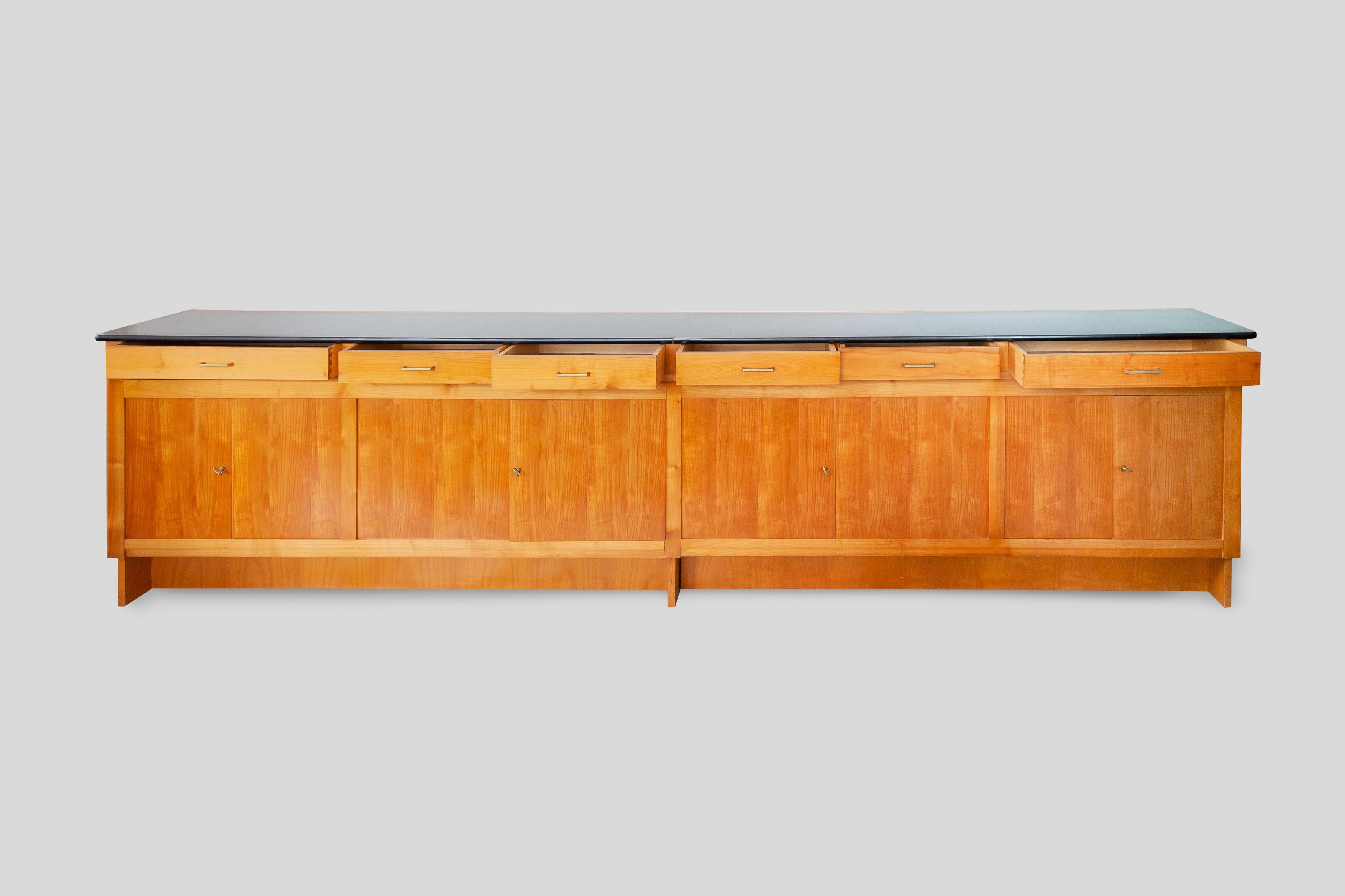 Straight-lined 1960s sideboard with four double doors and black laminated top. The large, beautifully sideboard was designed for a modern apartment in 1965 by an unknown artist. The front in ash wood consists of four compartments the left-hand