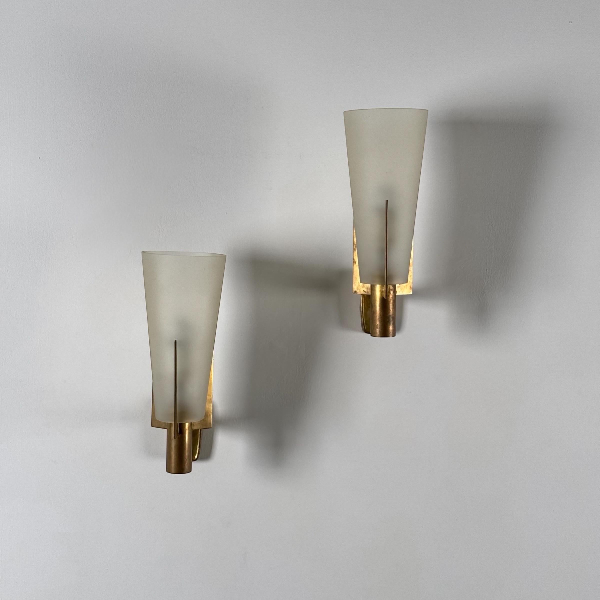 An early edition signed pair of Stilnovo wall sconces, Italy, circa 1950s. Each sconce features a frosted glass shade with a satiny surface that diffuses light with elegance, mounted on a brass frame of clean, angular lines. The brass retains its