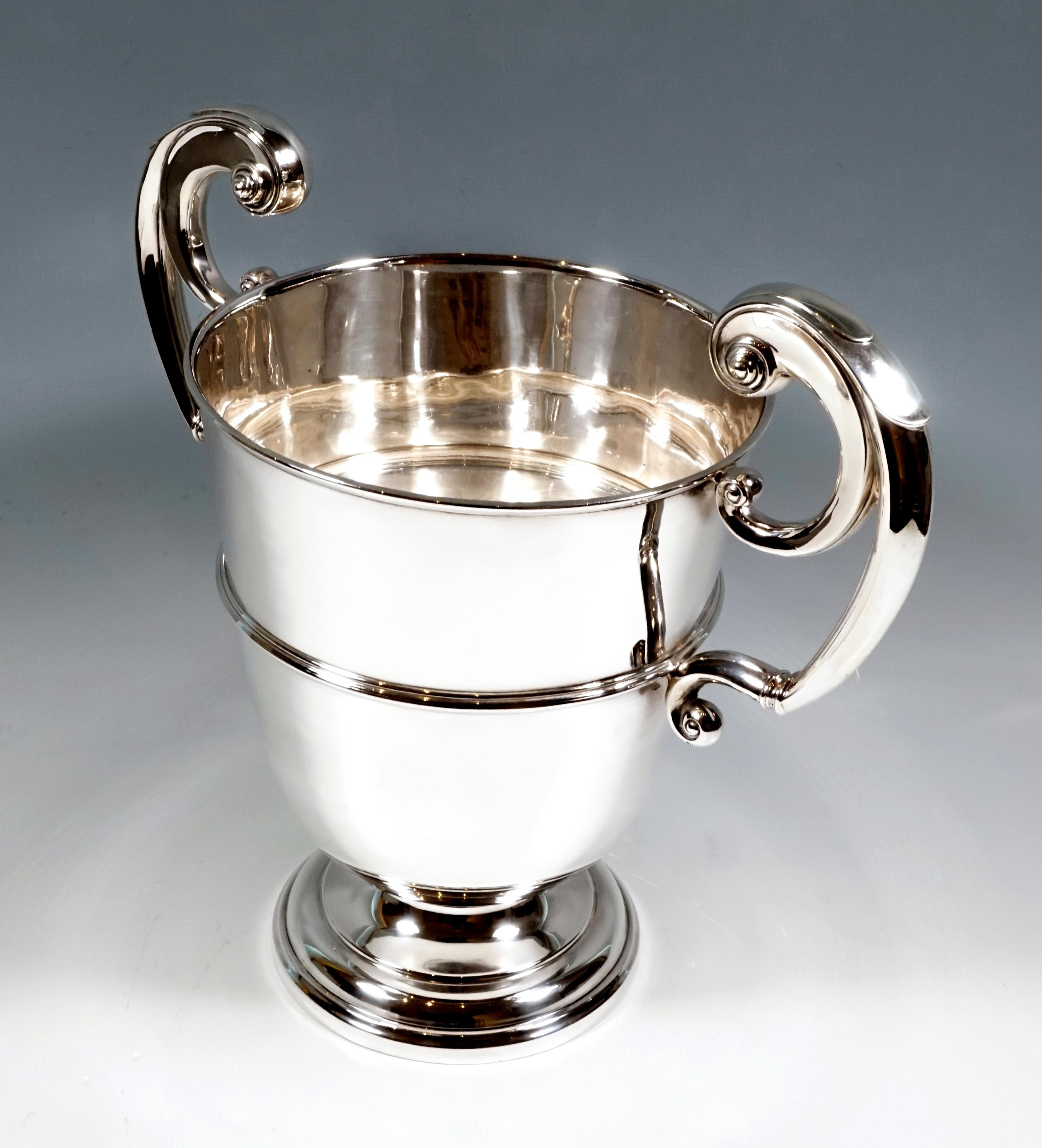 Elegant crater-shaped silver champagne cooler on an offset, stepped, round base with smooth, profiled walls and two large, raised volute-shaped handles.

925 silver

Hallmarks:
Master's sign 'WH&SSLD'- William Hutton & Sons Ltd., registered