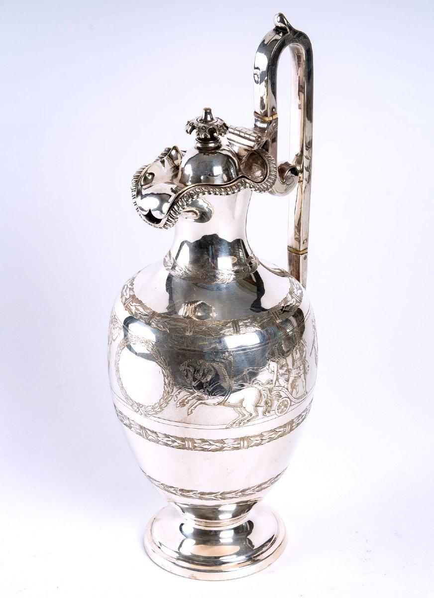 Of a very pure elegance here is a large ewer in silver metal, mounted on a pedestal, the ovoid body is finely chiselled with vegetable friezes and an antique frieze halfway up the body.

It is flanked by a majestic chiseled applique handle.
The
