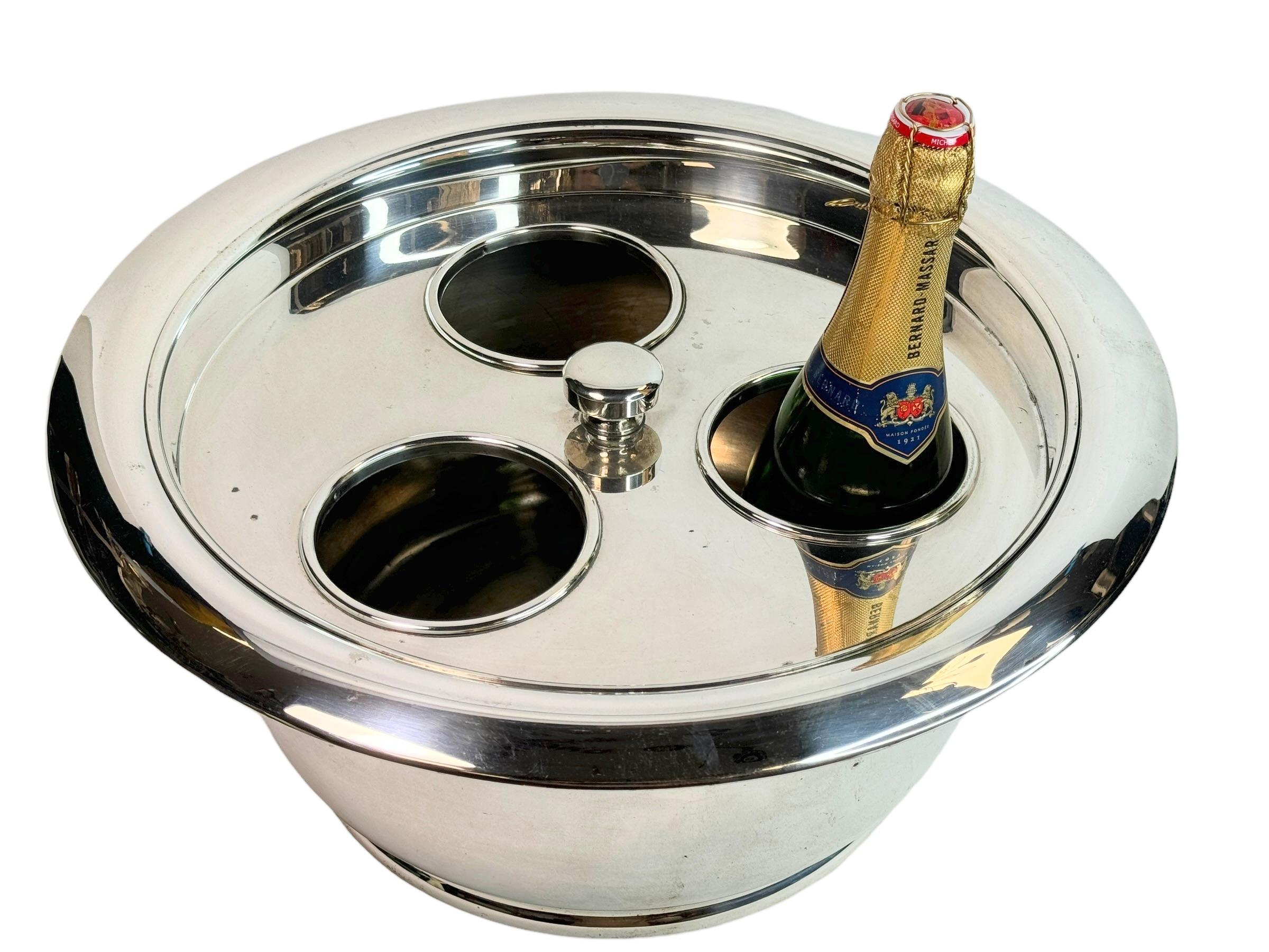 Un grande e imponente dispenser per champagne / centrotavola in metallo argentato. In ottime condizioni. Realizzato probabilmente negli anni '50 o più vecchi. Contrassegnato con il logo del produttore. 
Fonte in una vendita immobiliare a Tongern, in