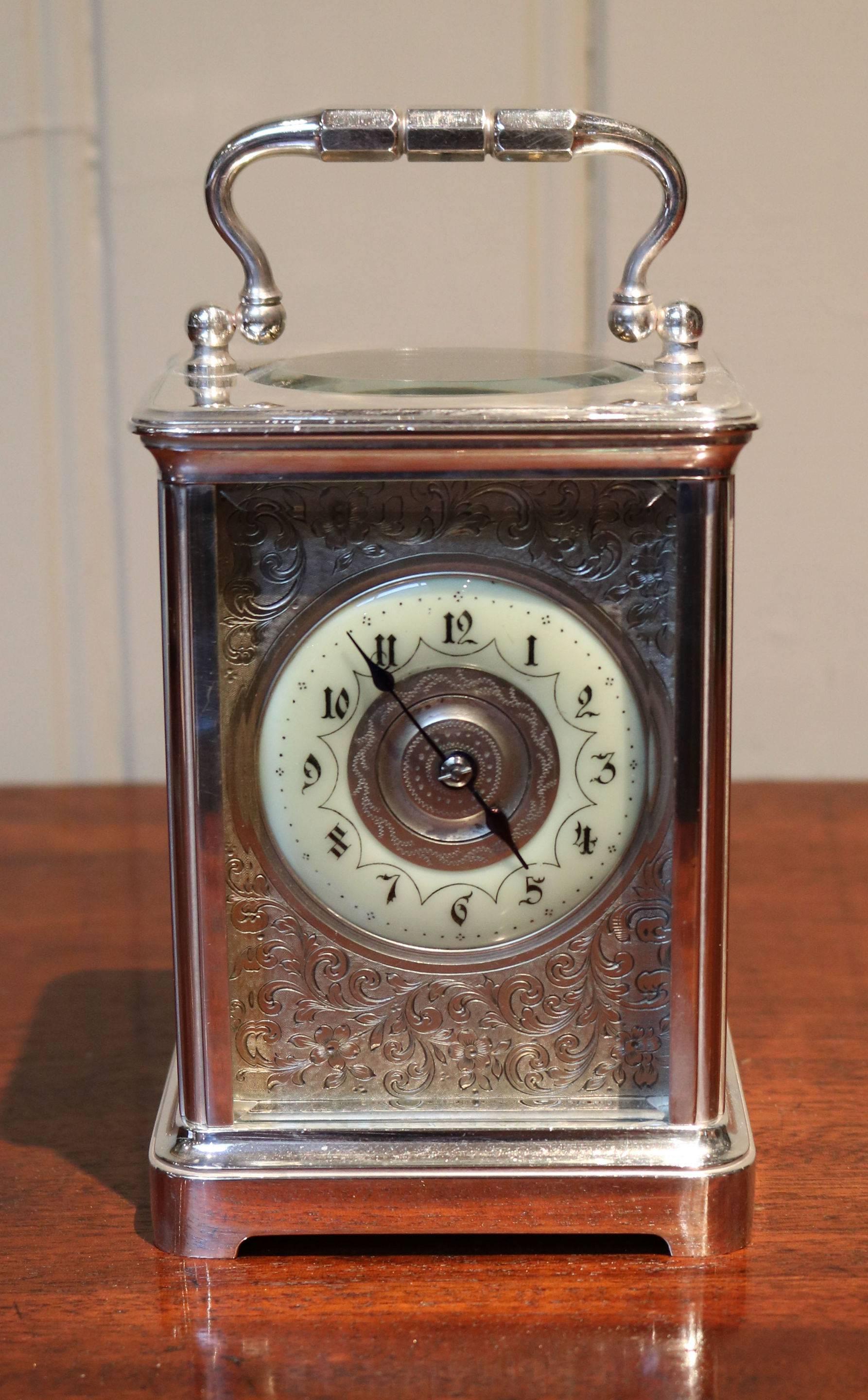 An attractive silver plated carriage clock dating to the late Victorian period. It has a corniche case, with a large bevel edge oval top window. It has an enamel chapter ring and a finely engraved floral dial mask. The 8 day movement has a cylinder