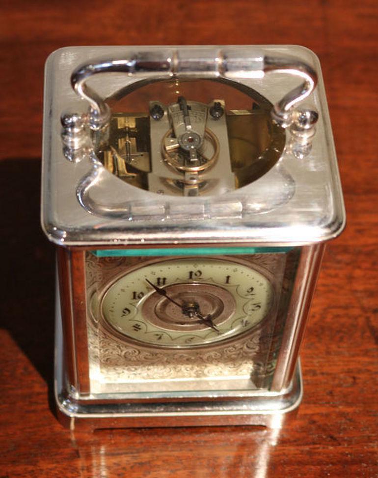 An attractive silver plated carriage clock dating to the late Victorian period. It has a corniche case, with a large bevel edge oval top window. It has an enamel chapter ring and a finely engraved floral dial mask. The 8 day movement has a cylinder