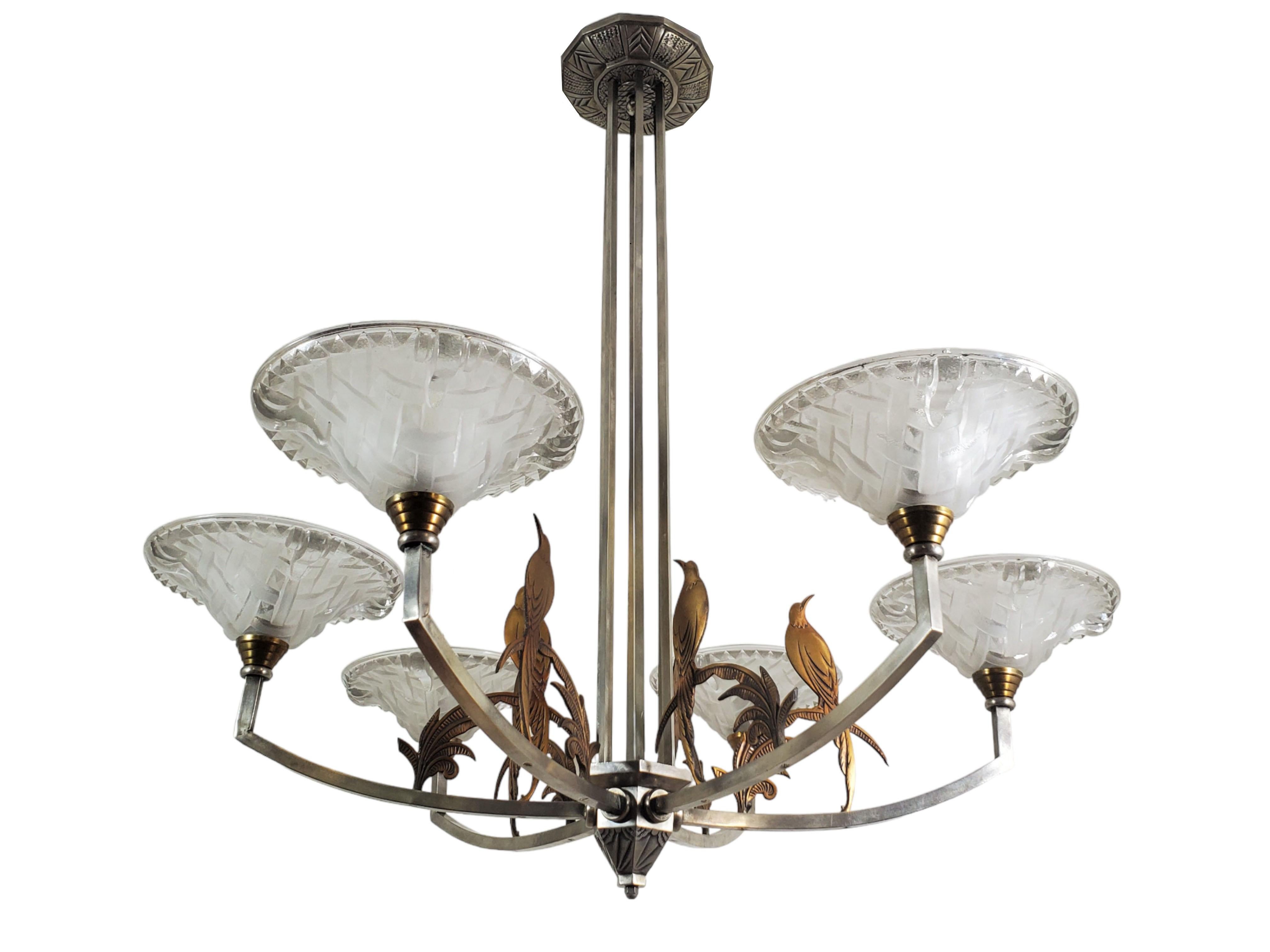 A unique and large French Art Deco chandelier attributed to Ezan with an intriguing two-tone finish, boasts six arms in a stunning arrangement. Each arm is adorned with exquisitely molded frosted art glass cups exhibiting a captivating geometric