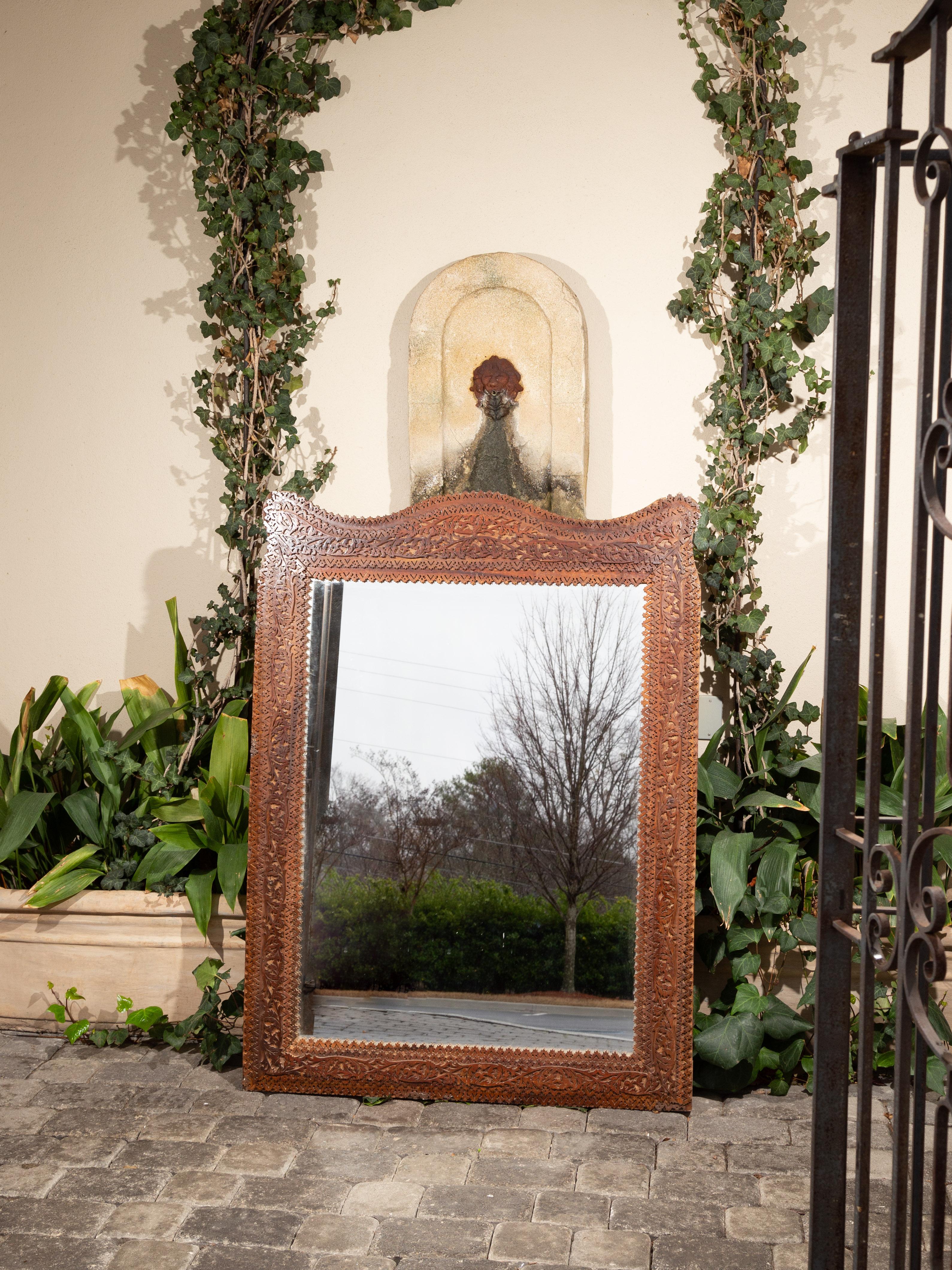 This Anglo-Indian mirror from the turn of the century features an exquisitely carved frame made of carefully cut-out motifs. The curvy crest contrasts nicely with the otherwise linear shape of the frame. The clear mirror provides perfect reflection.
