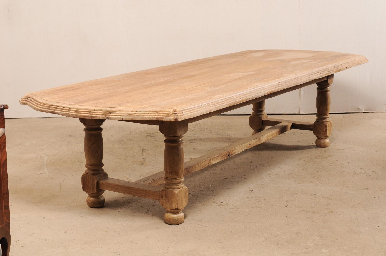 A large sized Anglo-Indian dining table fashioned from very sturdy reclaimed teak from the 19th century. This antique dining table has an overall rectangular-shaped top with rounded edges and subtly arched extensions at either far end. It is nicely
