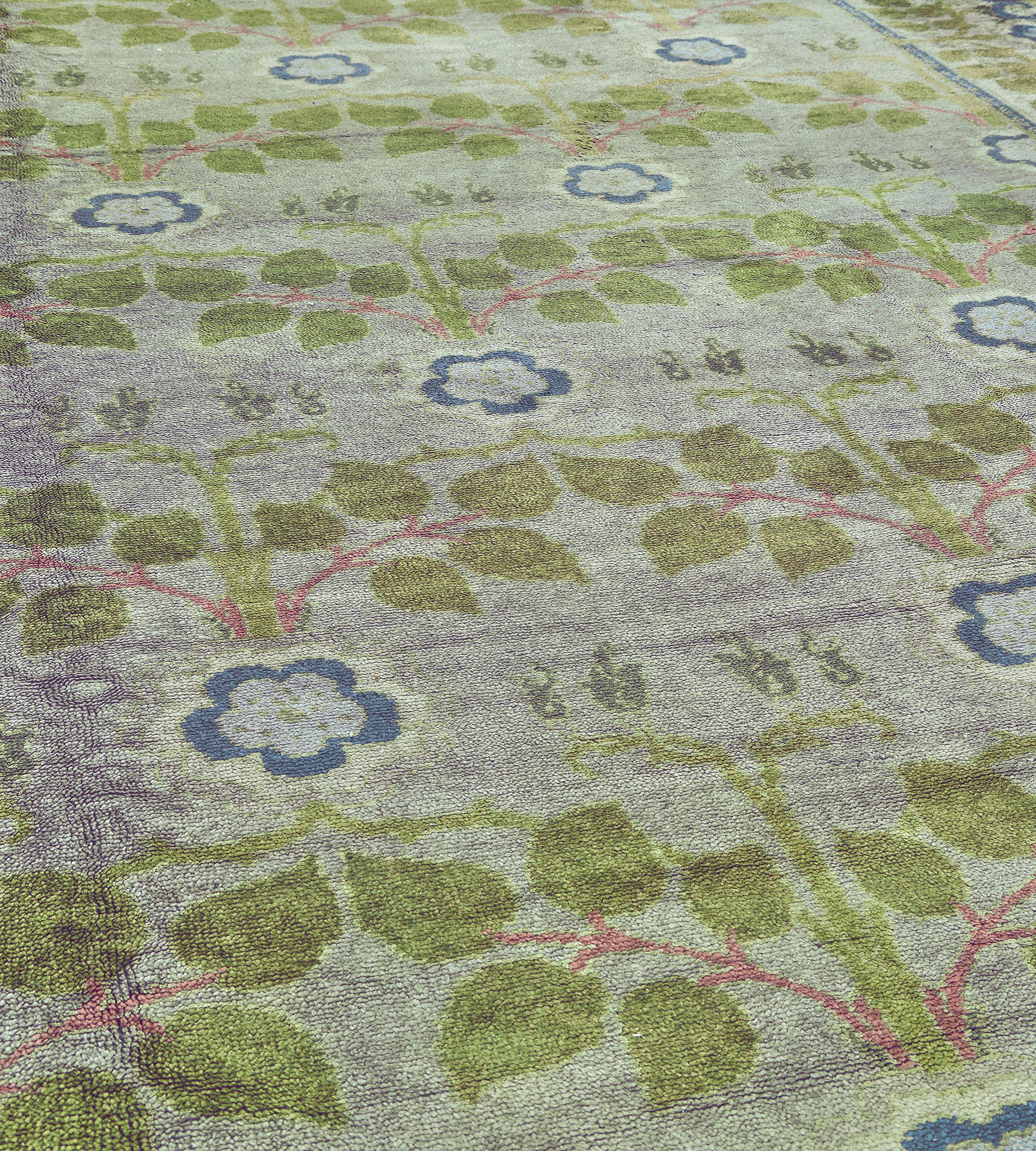 This handwoven antique Irish Donegal long rug has a pale blue field with an overall design with pairs of light green leafy sprays issuing from a shaded pink stem linked by a blue rosette, in a broad similar border between an inner narrow x-motif and