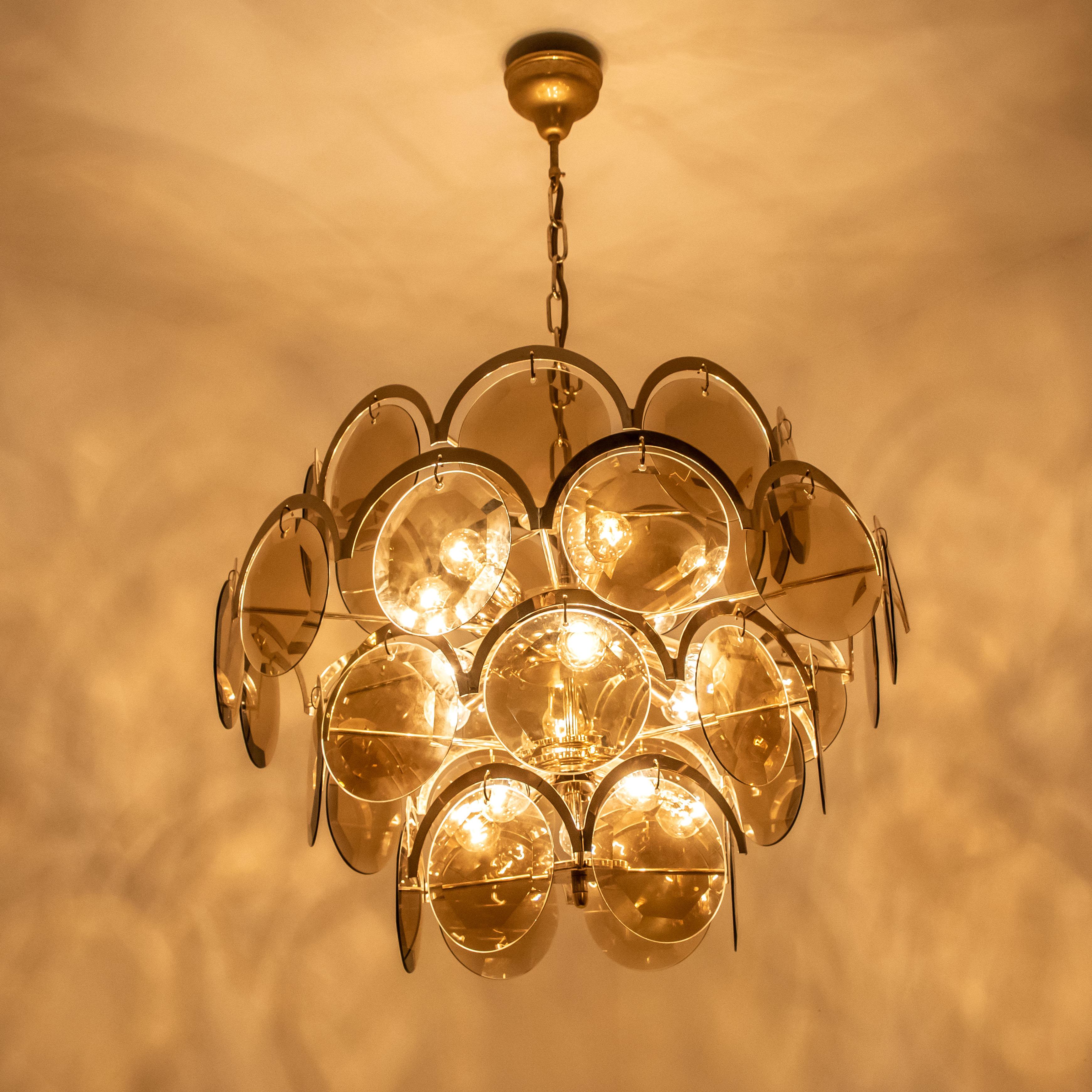 A gorgeous four tiers hanging light fixture, attributed to Vistosi with graduated tiers of smoked round facet chapped glass discs framed by half moon shaped brass. The chandelier is complete - no hook or glass disk is missing, with its original