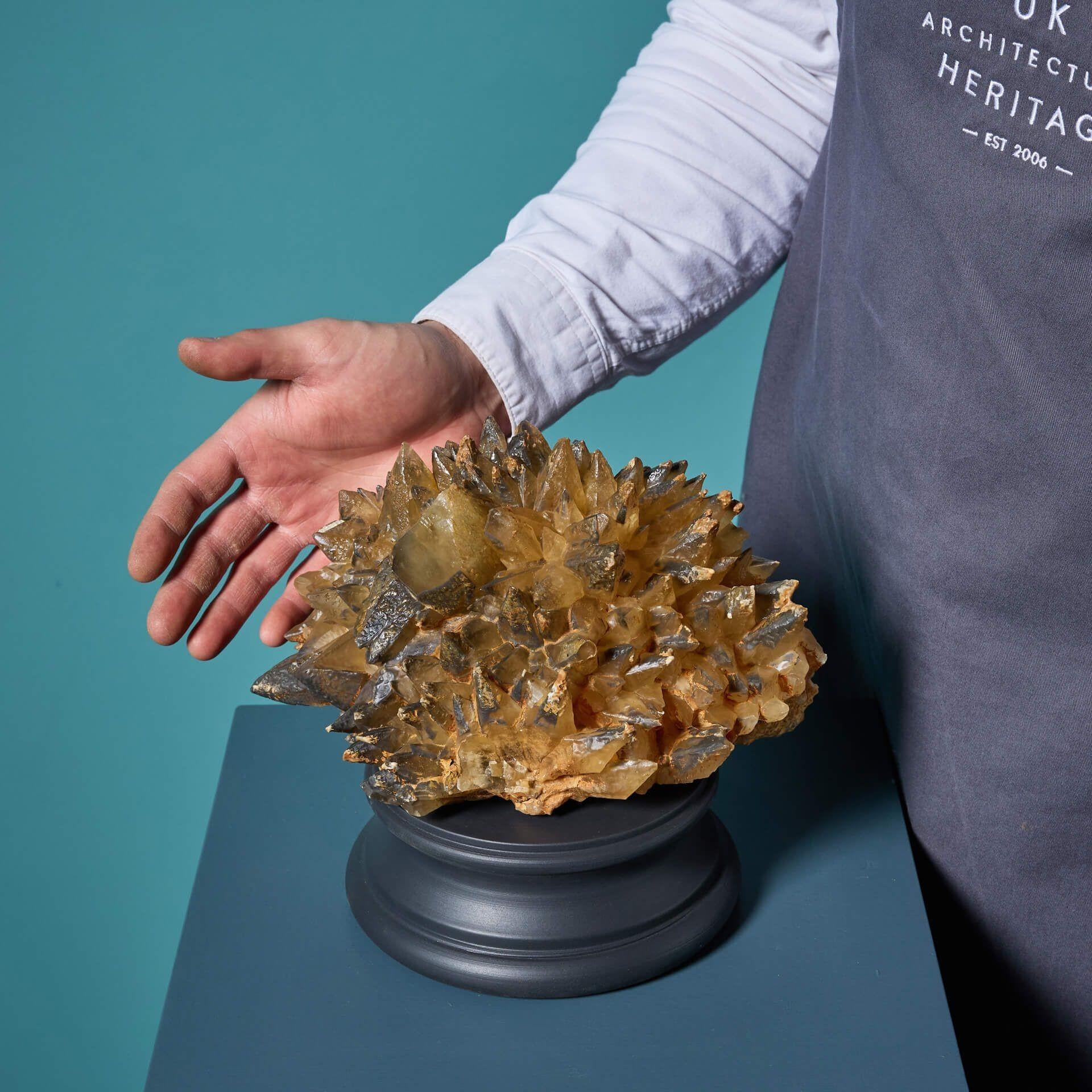 A large example of a naturally-formed smoky dogtooth calcite mineral specimen, presented on an exclusive plinth ready for interior display.

This natural calcite specimen is an excellent example of the dogtooth variety with golden scalenohedral