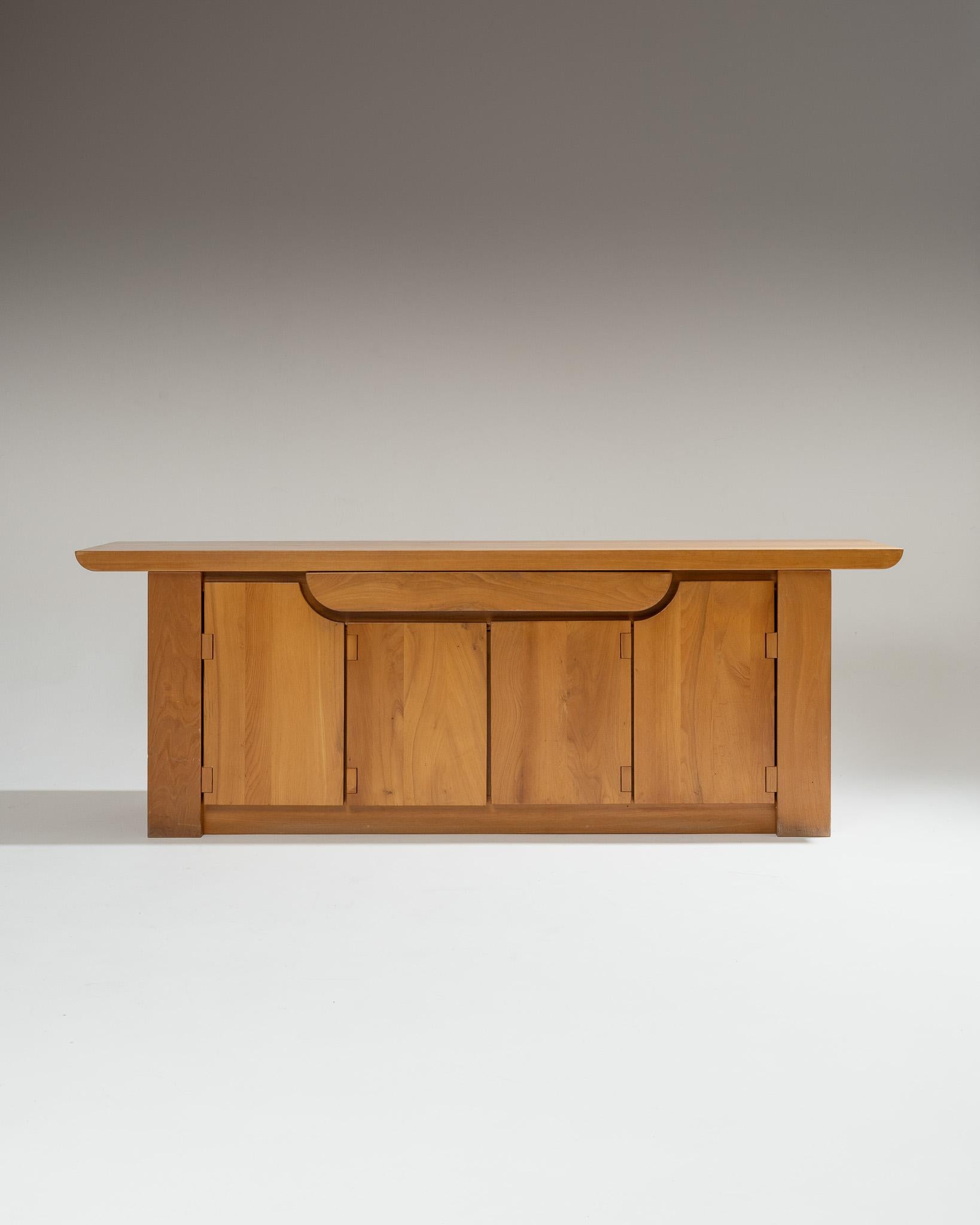 Buffet en orme massif dessiné par Luigi Gorgoni pour Roche Bobois dans les années 1980. Plateau épais sculpté en aile d’avion, quatre portes ouvrant sur étagères et tiroir central dissimulé. Charnières et détails en bois massif illustrant le travail