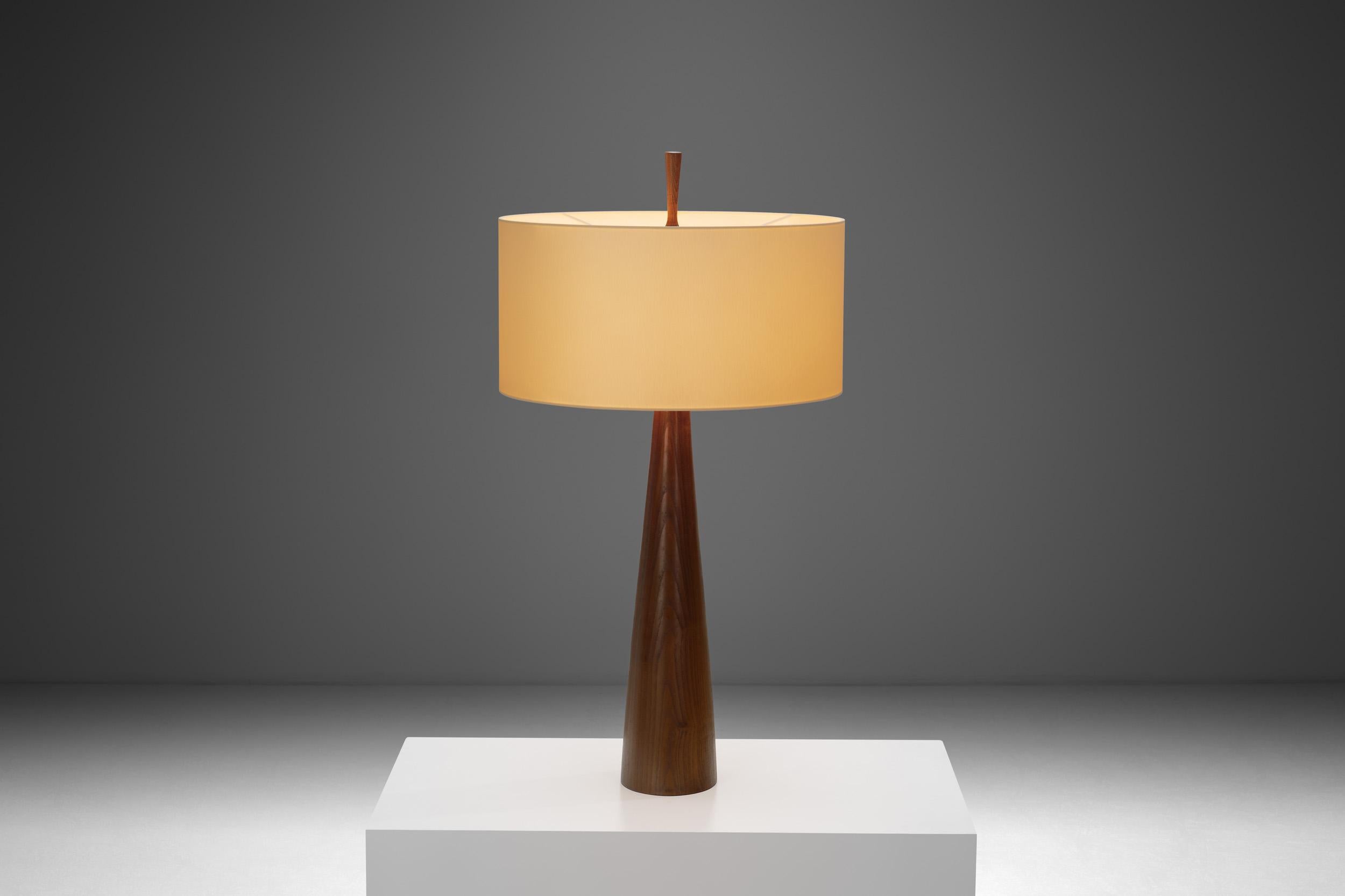 This large table lamp is a stunning example of the principles characteristic of mid-century modern design, crafted from solid walnut to highlight the natural beauty and unique grain of the wood. The lamp’s substantial size makes it a striking focal