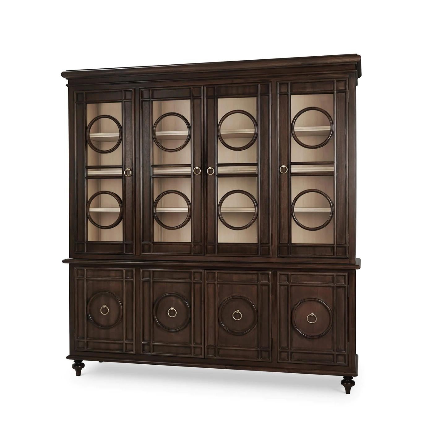 Crafted from mahogany and finished in a deep walnut tone, this sophisticated cabinet features glass-paneled doors adorned with circular motifs to the glass doors and lower panels. The symmetrical layout and form evoke the grandeur of traditional