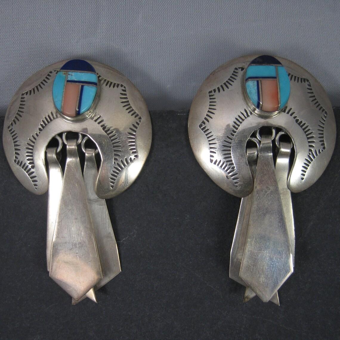 These large gorgeous earrings are sterling silver.
They are Navajo in origin and feature inlay in lapis, natural turquoise and pink spiny oyster.
Measurements: 1 1/2 by 2 1/2 inches
Weight: 22.7 grams
Marks: sterling
Condition: Excellent