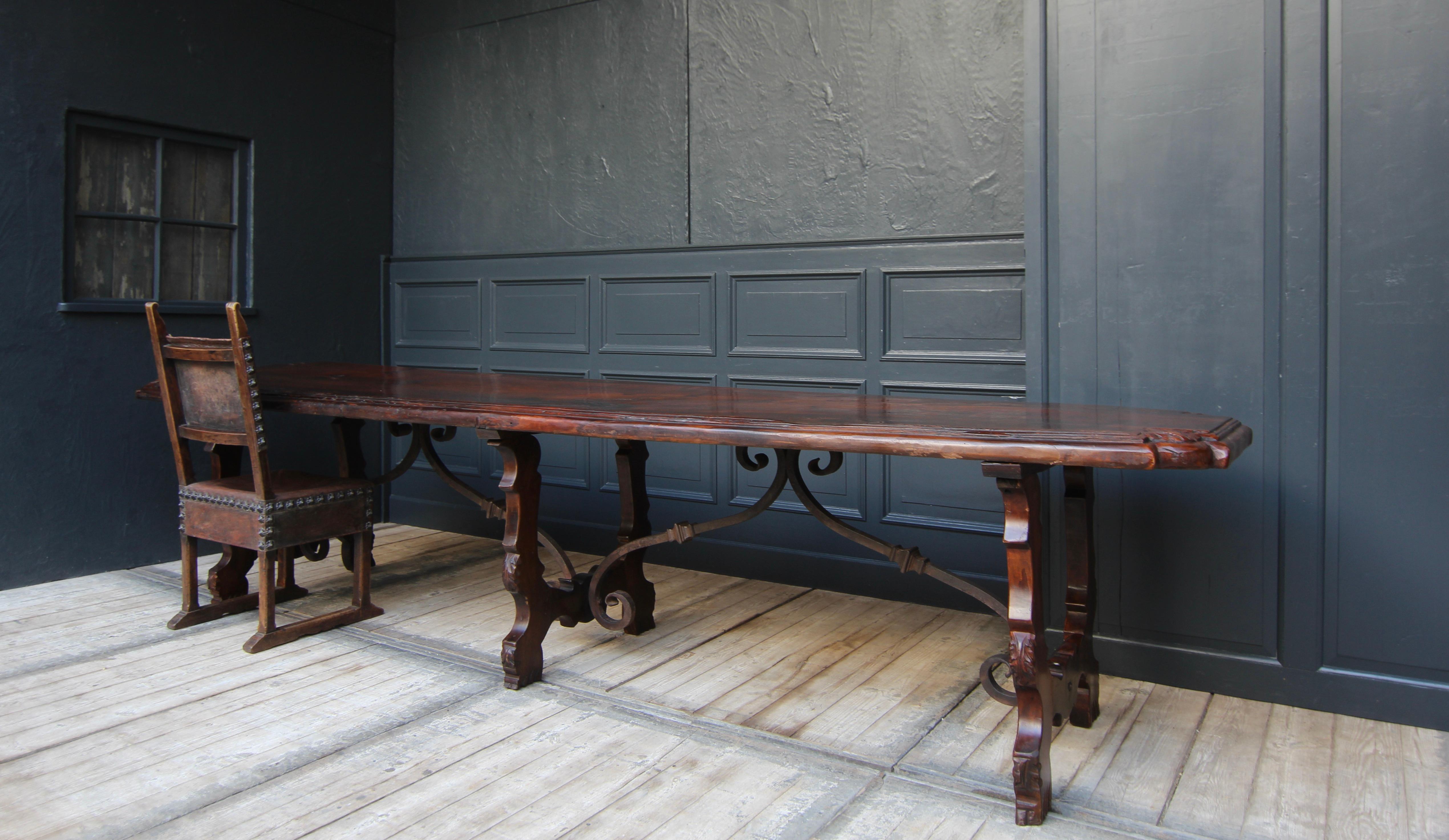 Large Spanish chestnut dining table in Baroque style. Presumably made in the early 20th century, partly using original parts from the 19th century.

Table frame on rectangular base, consisting of 3 carved trestles connected by ornate wrought-iron