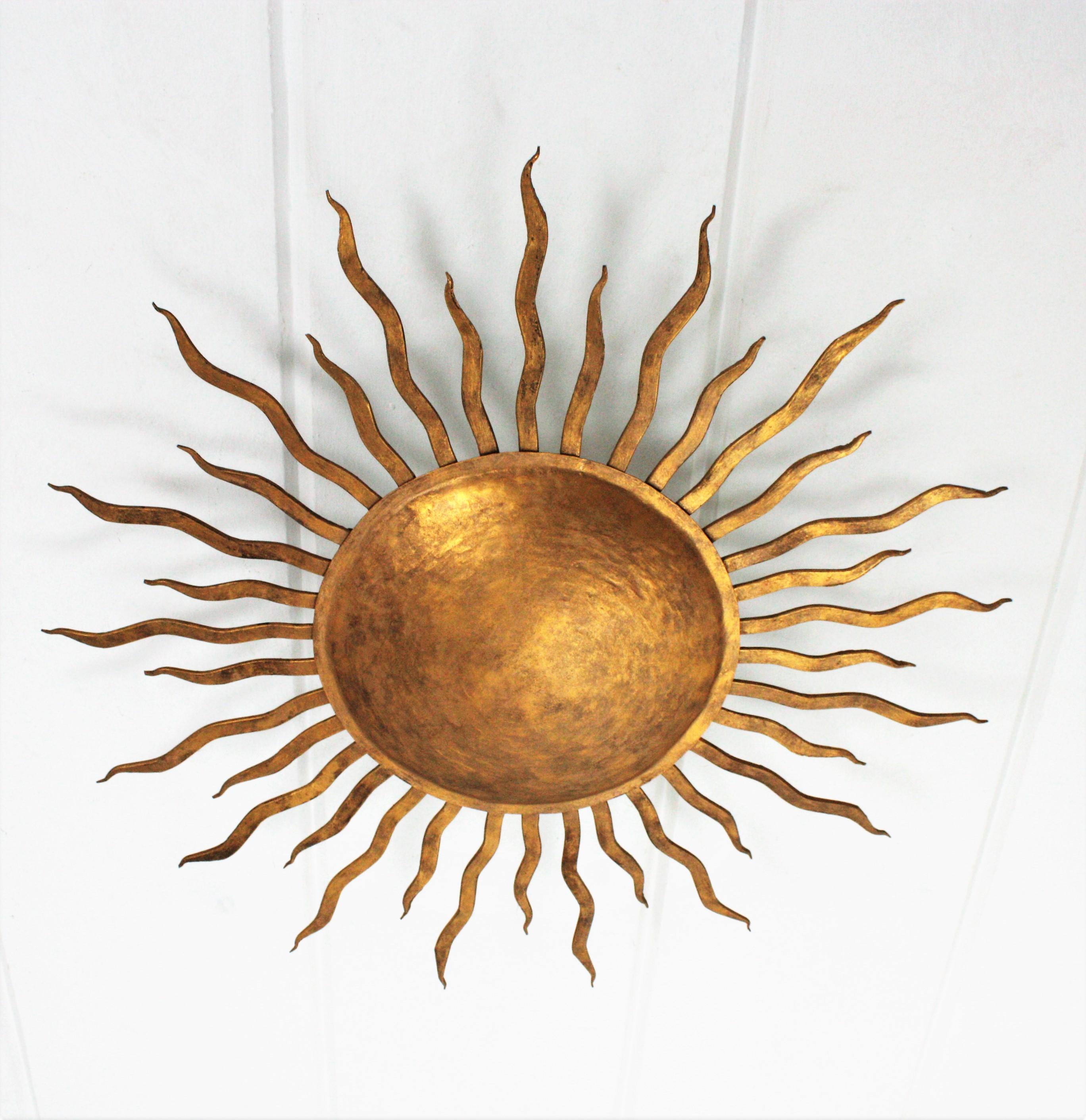 A beautiful hand-hammered sunburst flush mount with gold leaf finish made in wrought iron, Spain, 1950s.
It has thick rays in two sizes surrounding the central large sphere.
It can be placed flush mounted or as a pendant or chandelier hanging on a