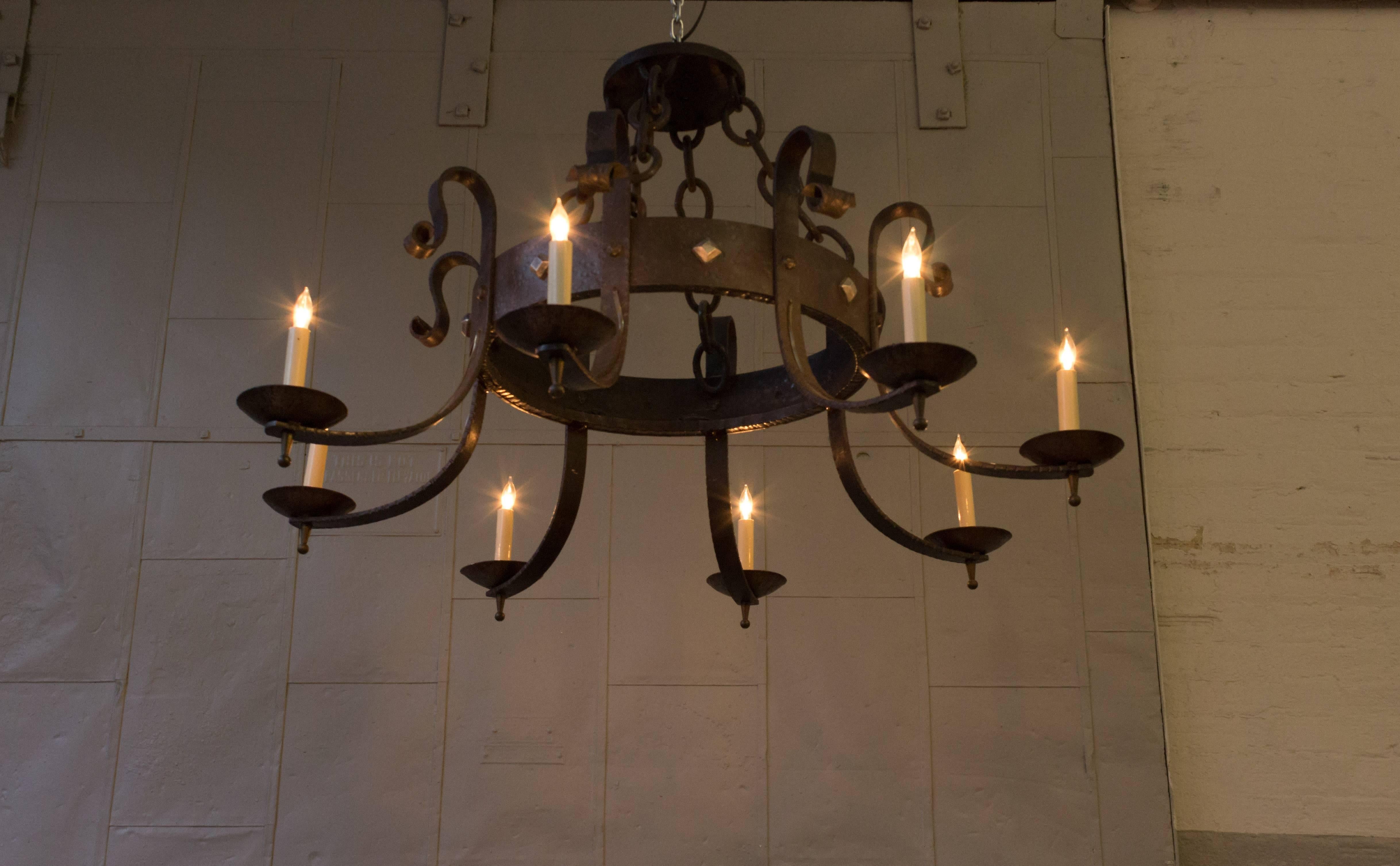 This exceptional gothic style Spanish eight-arm wrought iron chandelier boasts a distinctive hammered finish, a sturdy heavy linked chain, and an exquisite brass finial detail adorning the bottom of the lights. This remarkable piece is in very good
