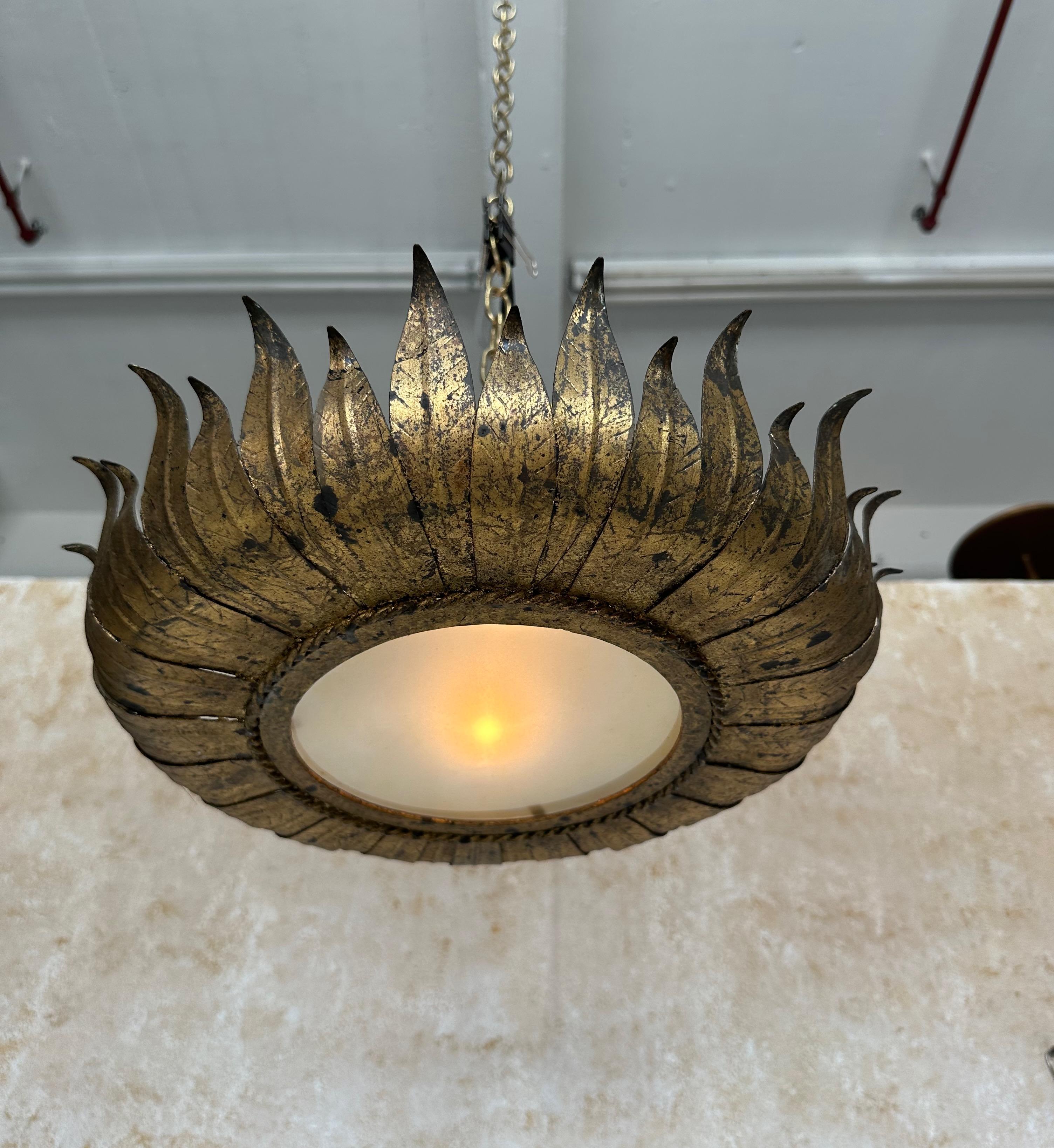 This large Spanish 1950s gilt metal ceiling fixture features a sweeping crown array of alternating long and short leaves surrounding a circular frame with a braided border that holds the frosted glass center. The beautiful hand applied rich gold