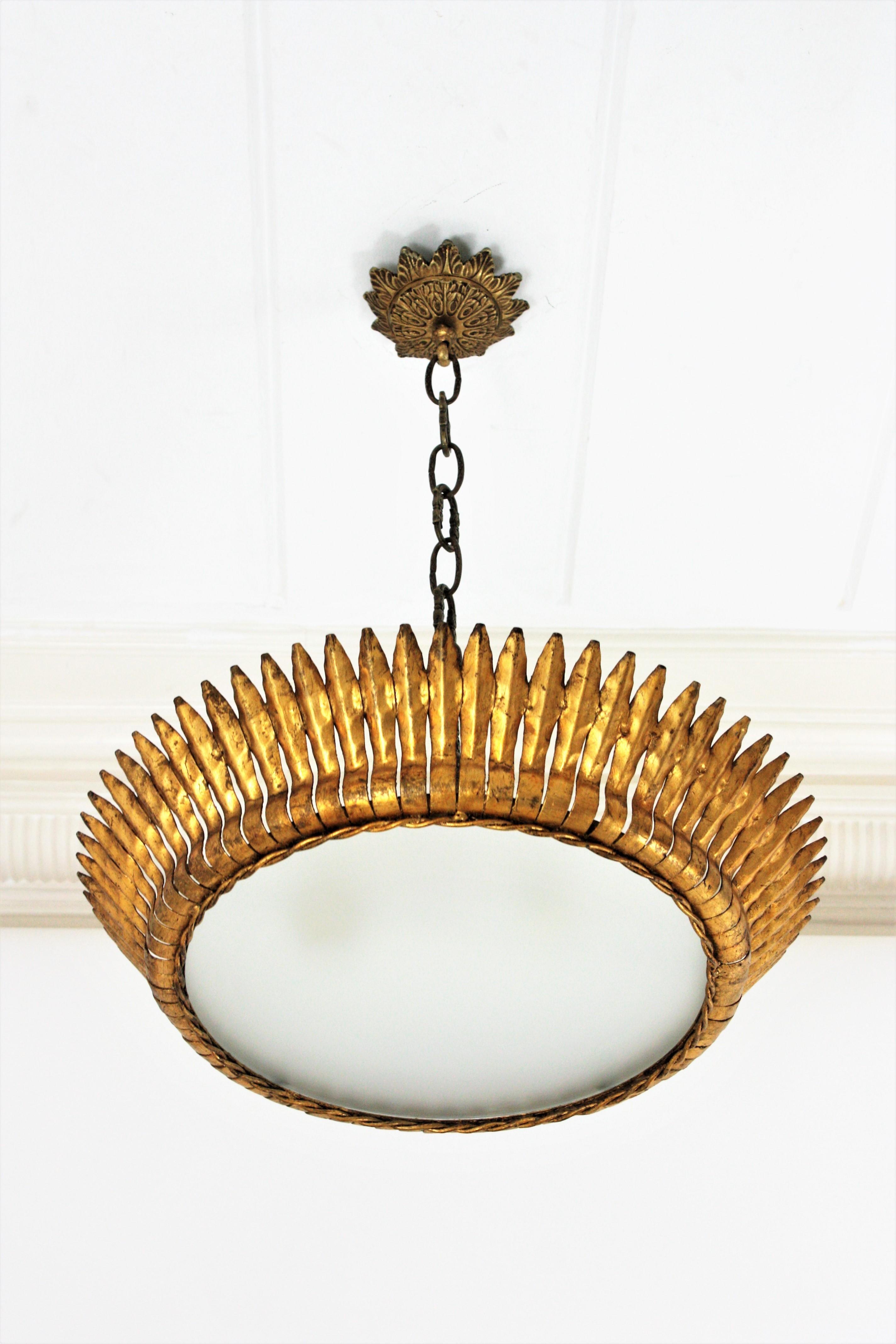 Mid-Century Modern gilt iron crown sunburst flushmount or pendant with leaf motifs surrounding a central frosted glass diffuser, Spain, 1950s.
Handcrafted in hammered iron with gold leaf finishing.
It has a twisted iron rope surrounding the glass