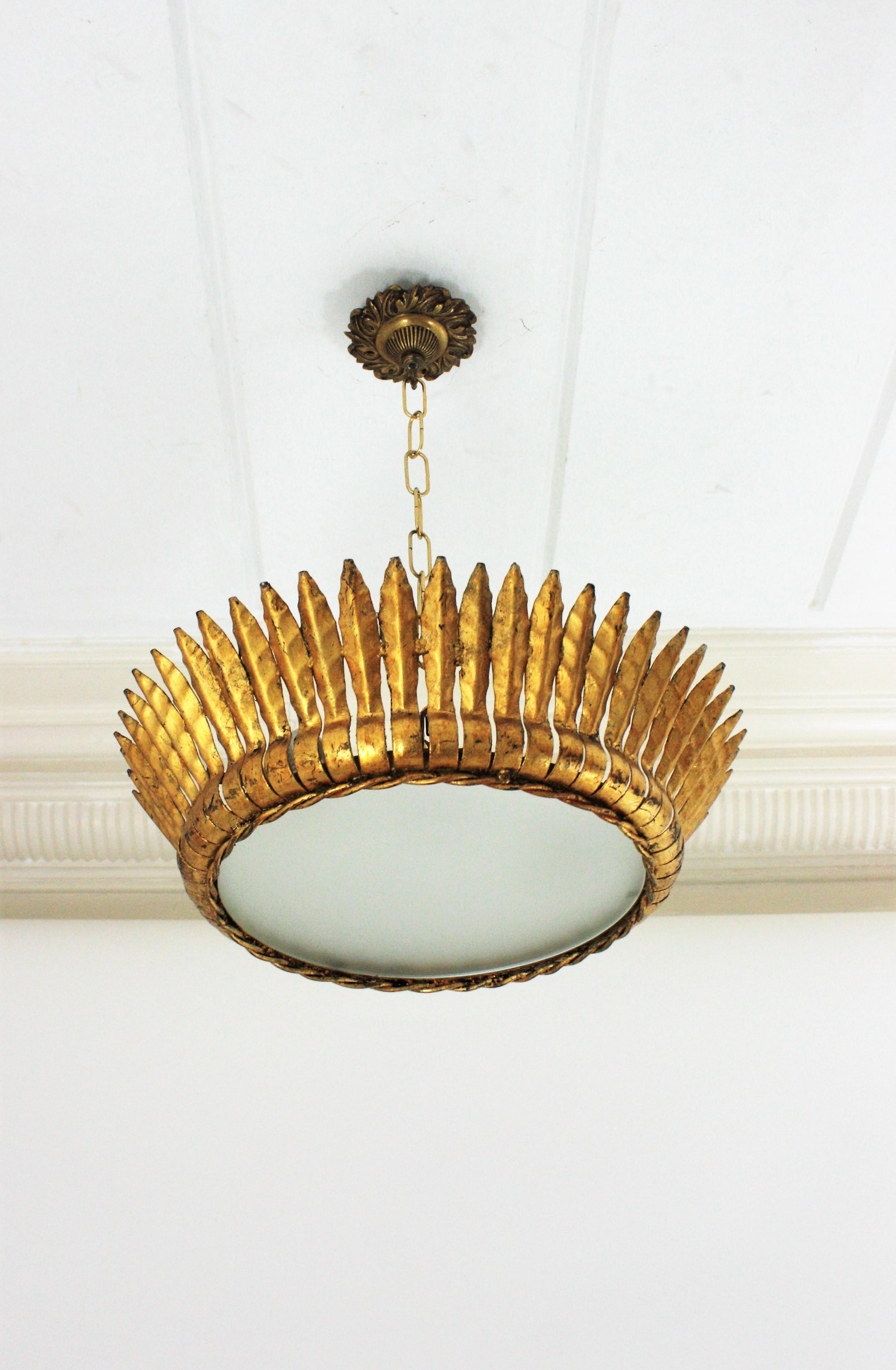 Mid-Century Modern gilt iron crown sunburst flushmount or pendant with leaf motifs surrounding a central frosted glass diffuser, Spain, 1950s.
Handcrafted in hammered iron with gold leaf finishing.
It has a twisted iron rope surrounding the glass