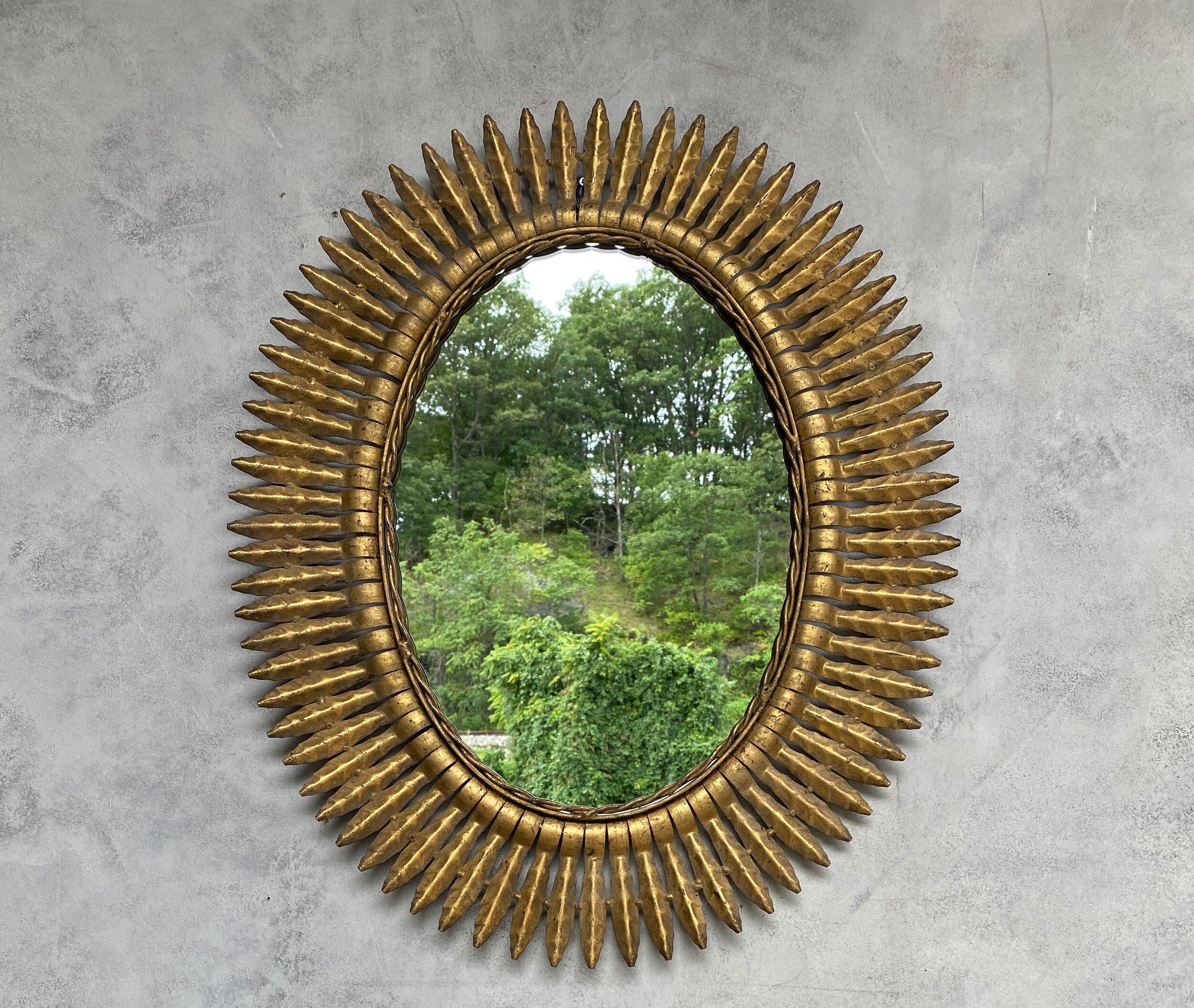 A large oval gilt metal sunburst mirror with small pointed rays arranged to form a tightly fitted frame, Spanish, 1950s. We recently added a felt backing to the mirror to give it more protection and a finished look. Very good vintage