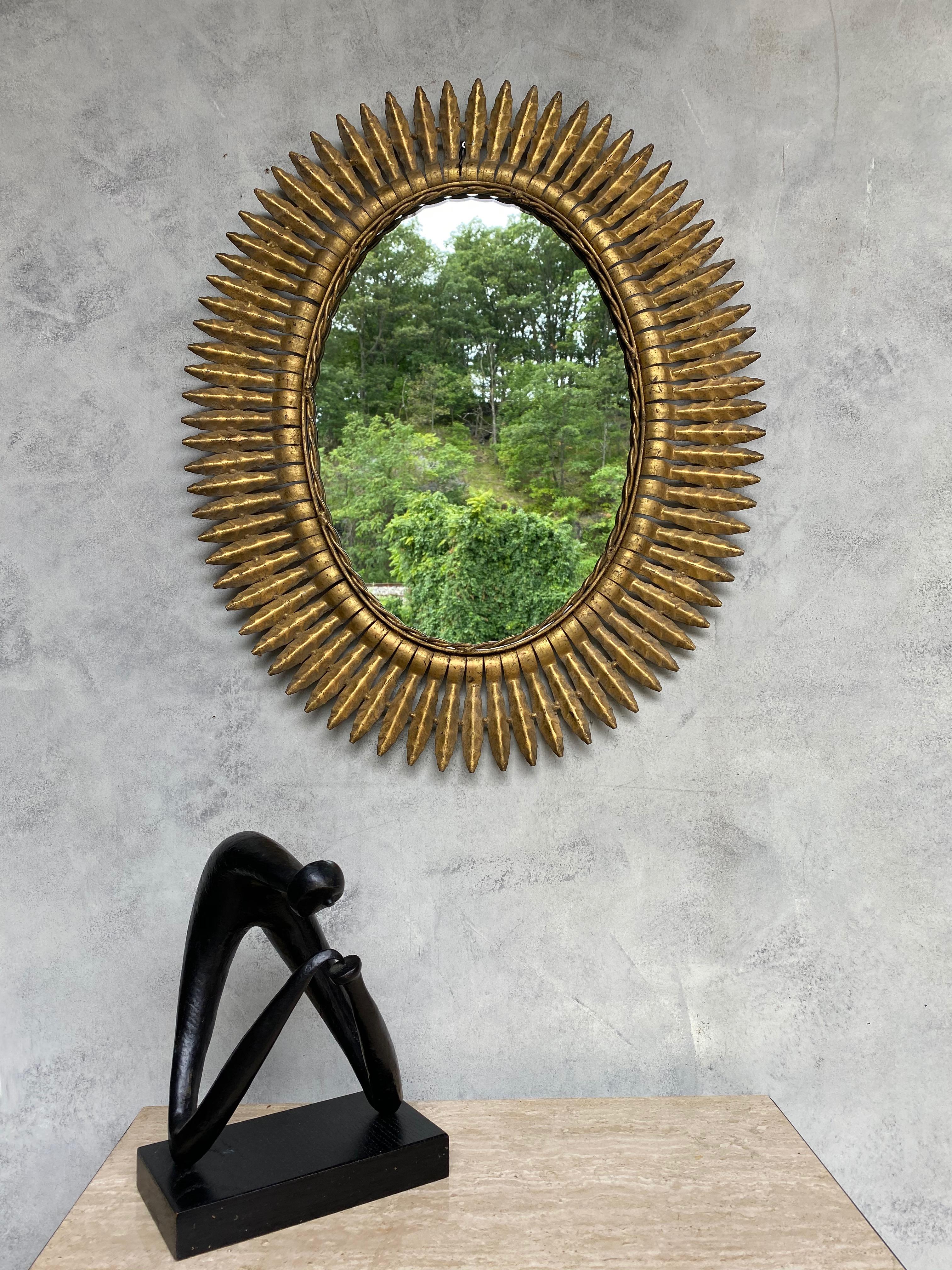 A large oval gilt metal sunburst mirror with small pointed rays arranged to form a tightly fitted frame, Spanish, 1950s. We recently added a felt backing to the mirror to give it more protection and a finished look. Very good vintage condition.
 