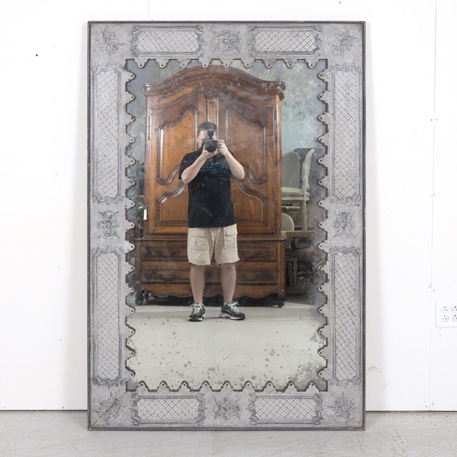An impressive Spanish mirror having a hand-painted lattice and stylized florets design handcrafted of reclaimed metal and wood with light crazing to the mirror glass. This large mirror features a scalloped interior edge and has a beautiful patina.
