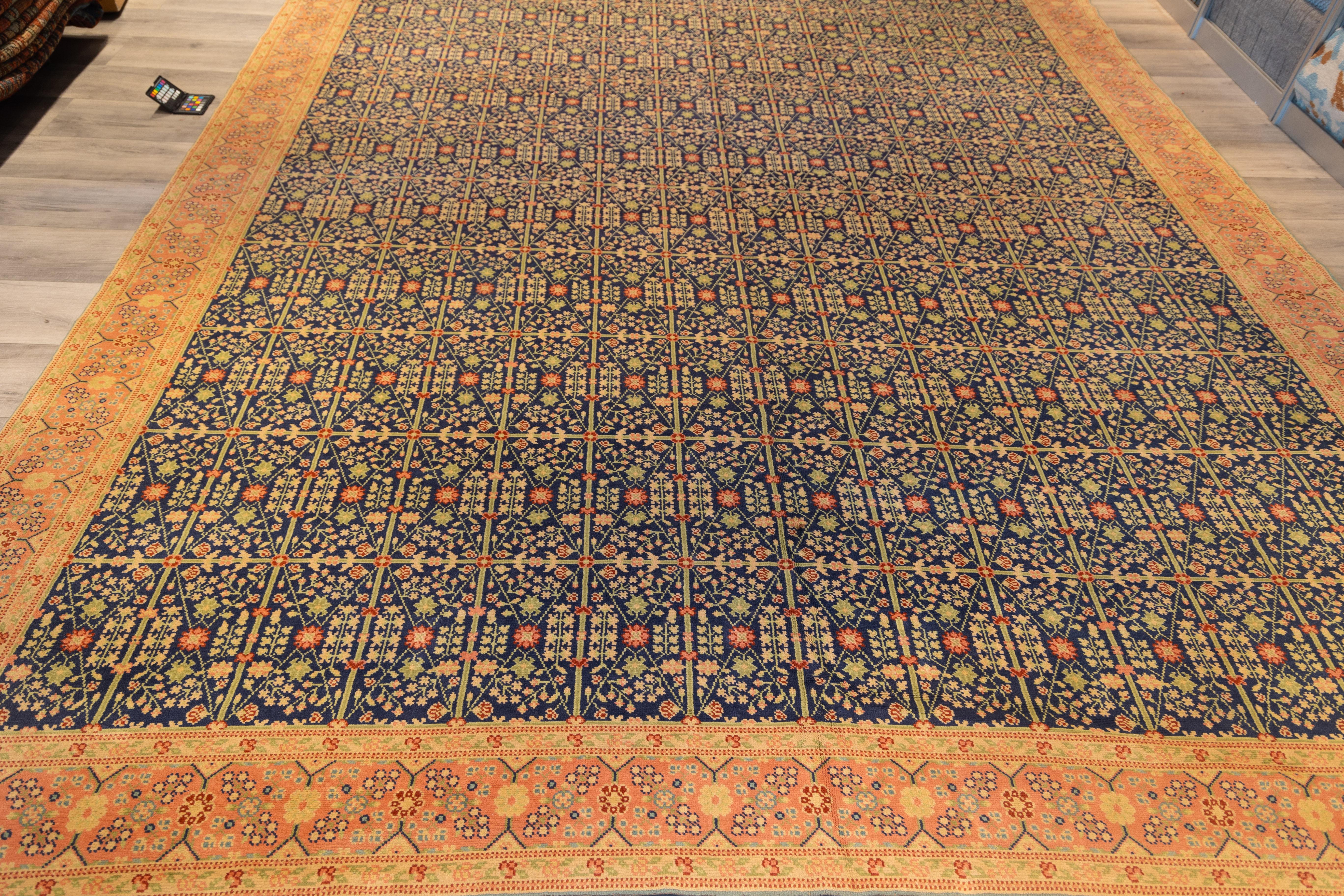 Elegant 1920s Spanish carpet showcases a striking allover latticework pattern rendered in deep indigo, saffron, and coral tones. Each compartment is meticulously filled with stylized floral motifs and rosettes, arranged in rhythmic precision that