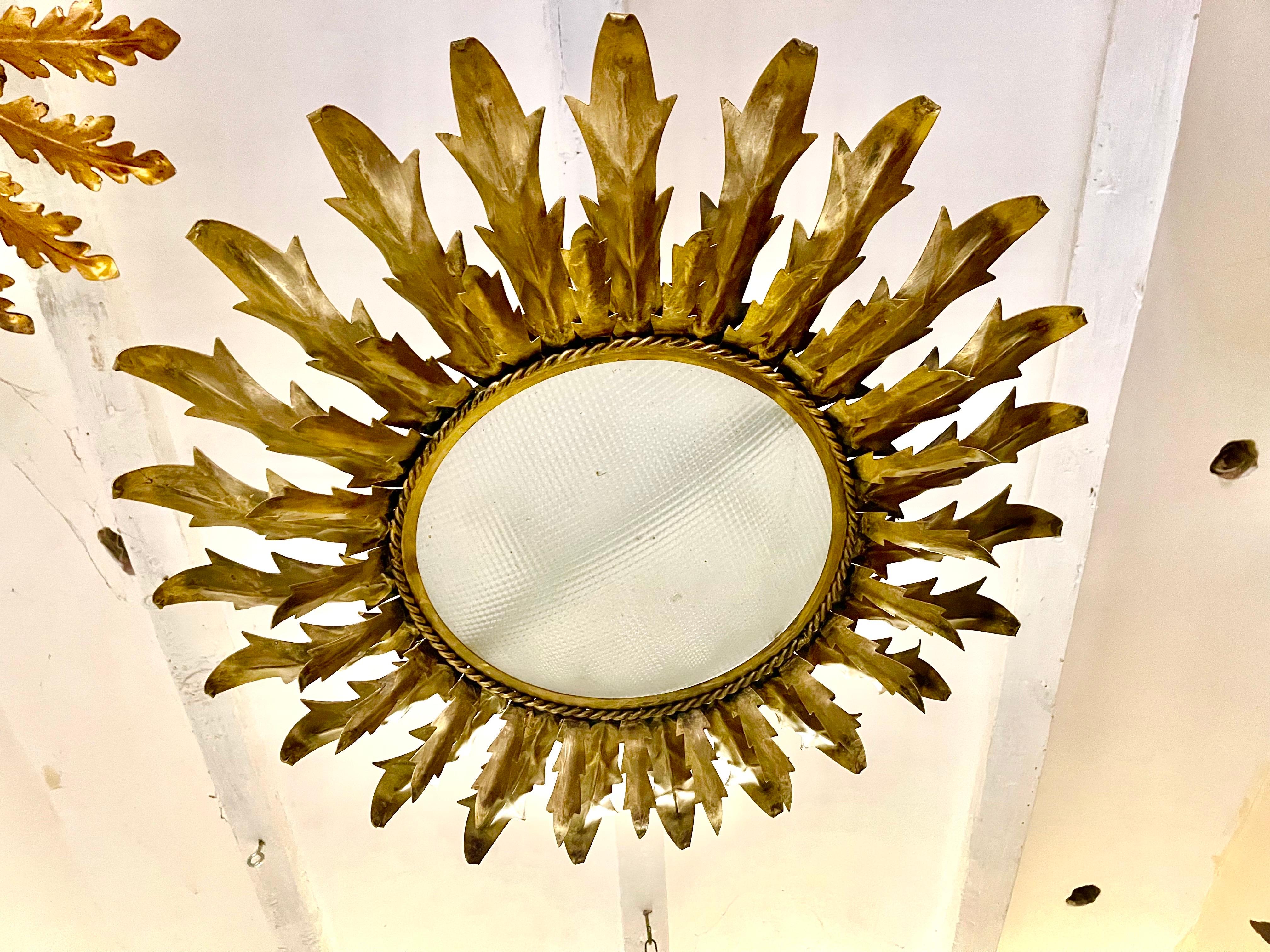 Large Spanish sunburst light in gilt metal and frosted glass ; white ; orange........other color
 Spain, 1950s. Midcentury antique gilt iron frame or pendant with laurel leaf motifs surrounding a central frosted glass diffuser. Handcrafted in
