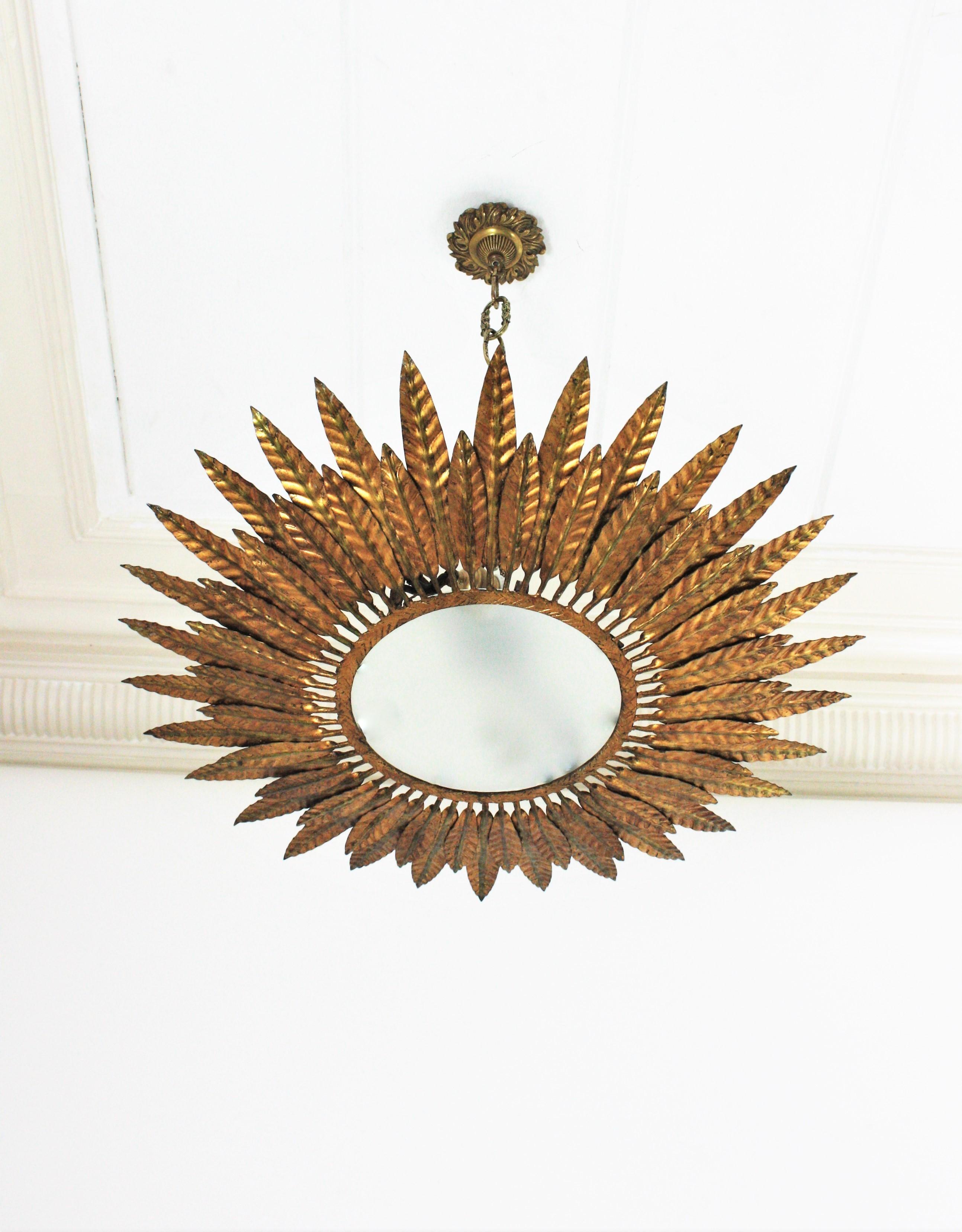 Mid-Century Modern gilt iron sunburst flush mount or pendant with leaf motifs surrounding a central frosted glass diffuser, Spain, 1950s.
Handcrafted in hammered iron with gold leaf finishing.
Nice aged patina and glamorous original gold leaf