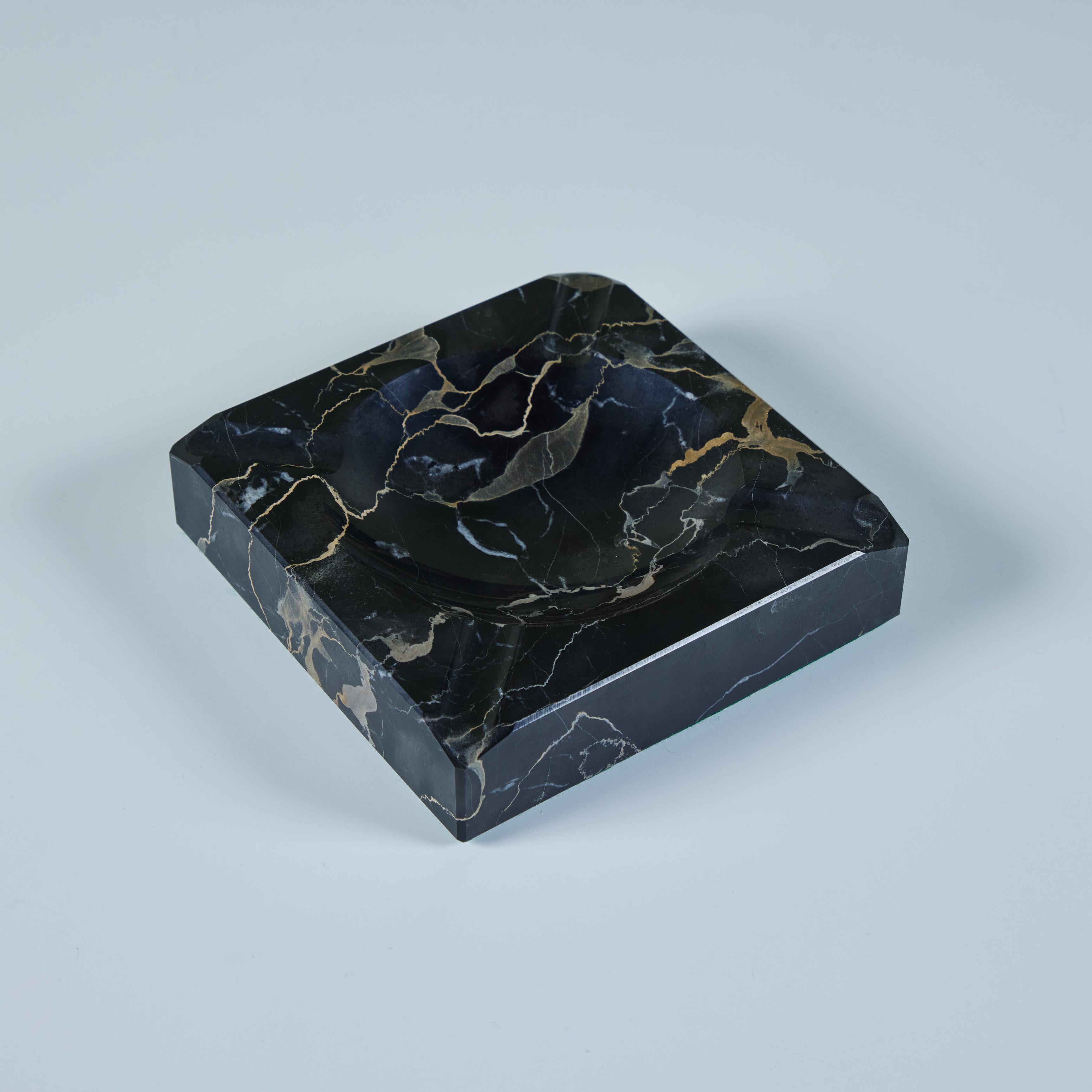 Square marble ashtray in a polished black marble with gray and tan veining. The piece has a circular well, and four routed indentations at each corner.

Dimensions 
6