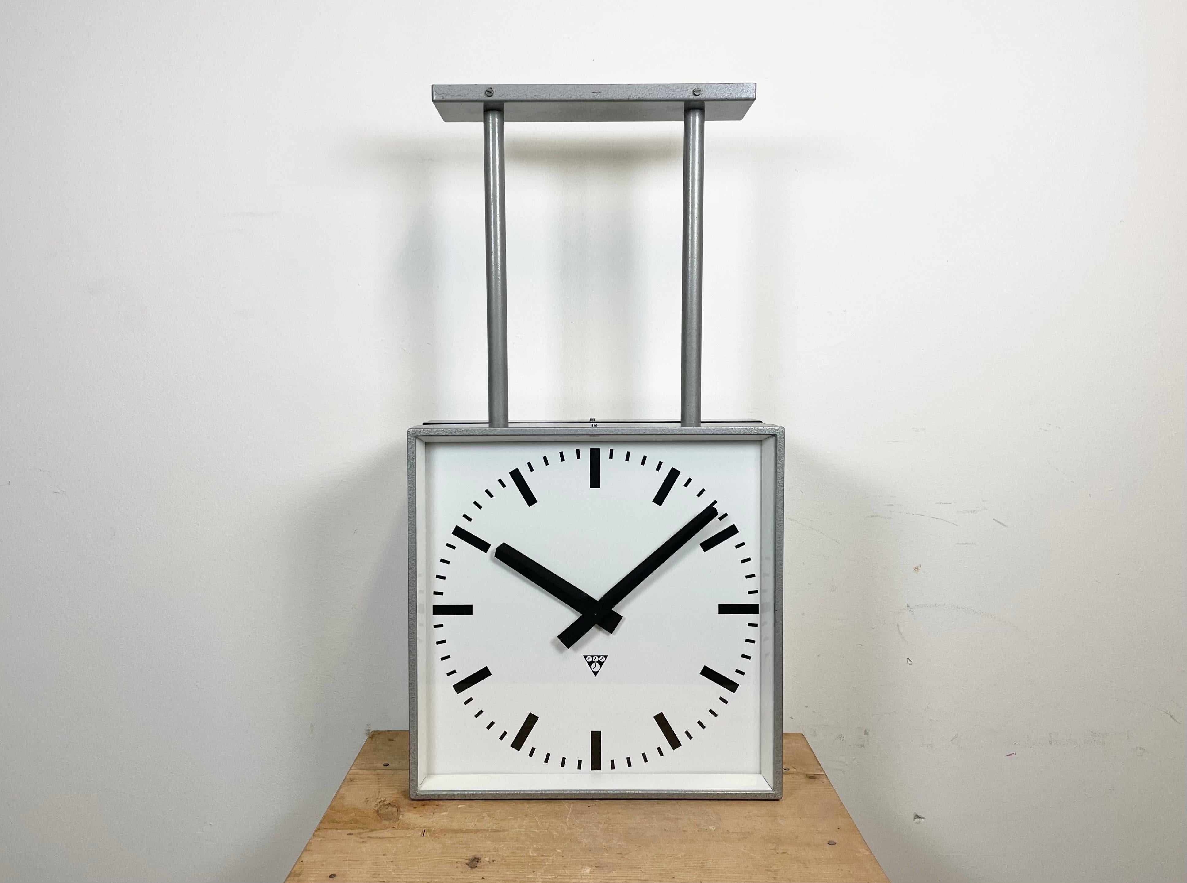This square double-sided railway, school or factory clock was produced by Pragotron, in former Czechoslovakia, during the 1970s. The piece features a grey hammerpaint metal body, a clear glass cover, and an aluminum dial and hands. The clock has