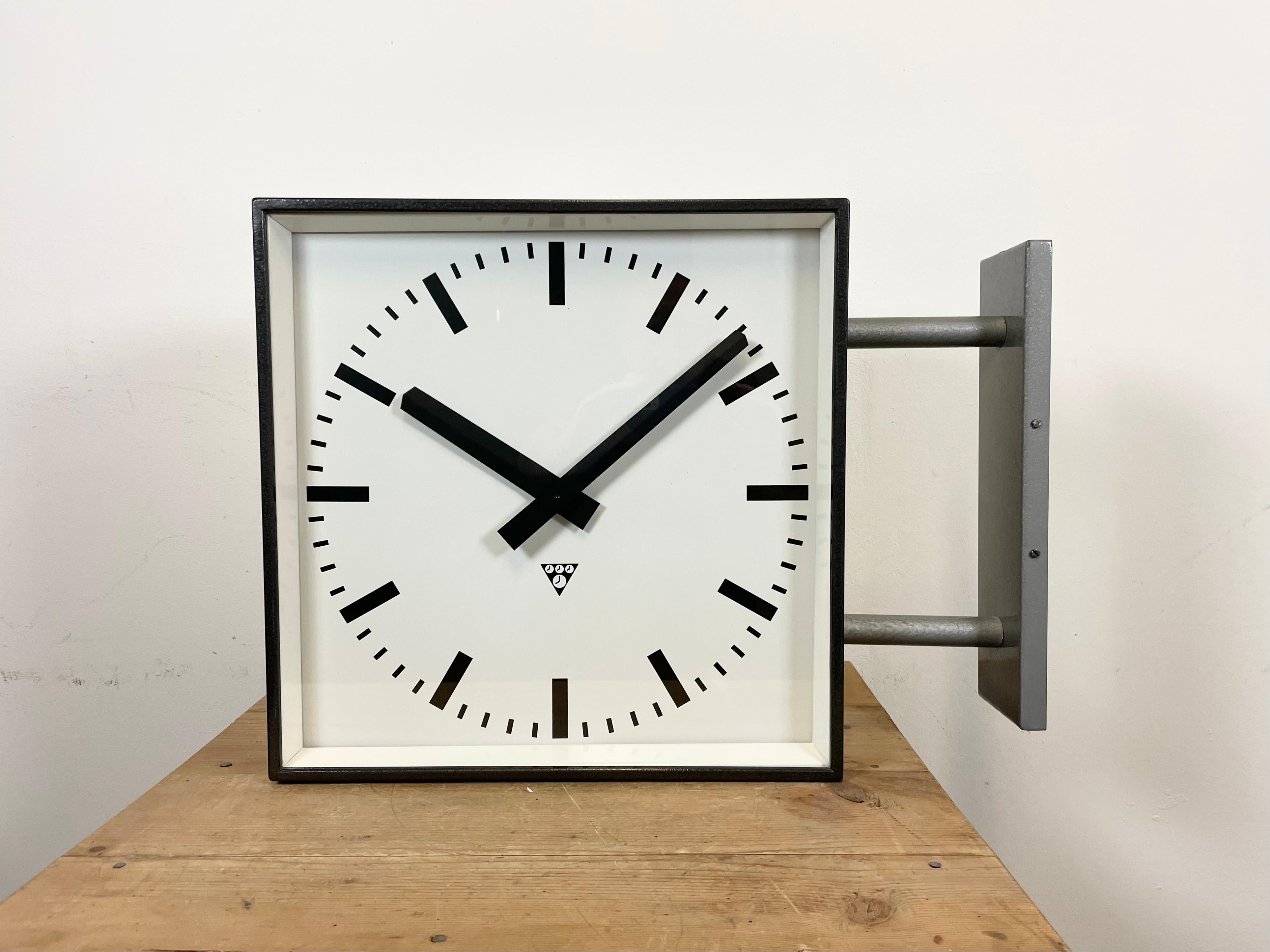 This square double-sided railway, school or factory wall clock was produced by Pragotron, in former Czechoslovakia, during the 1970s. The piece features a grey hammerpaint metal body, a clear glass cover, and an aluminum dial and hands. The clock