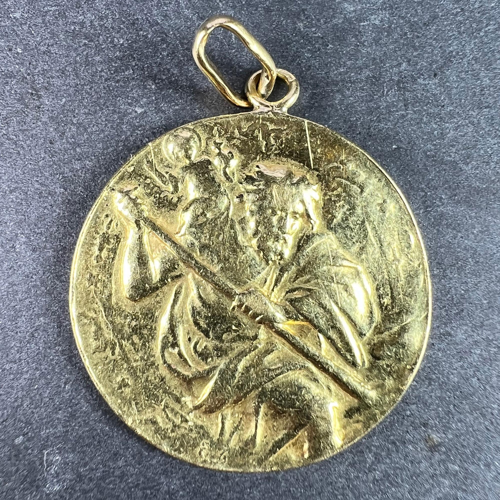 A large 18 karat (18K) yellow gold charm pendant designed as a medal depicting St Christopher as he carries the infant Christ across a river, the reverse with the phrase 'REGARDE ST CHRISTOPHE ET PUIS VA T'EN RASSURE' above a cross with an engraved