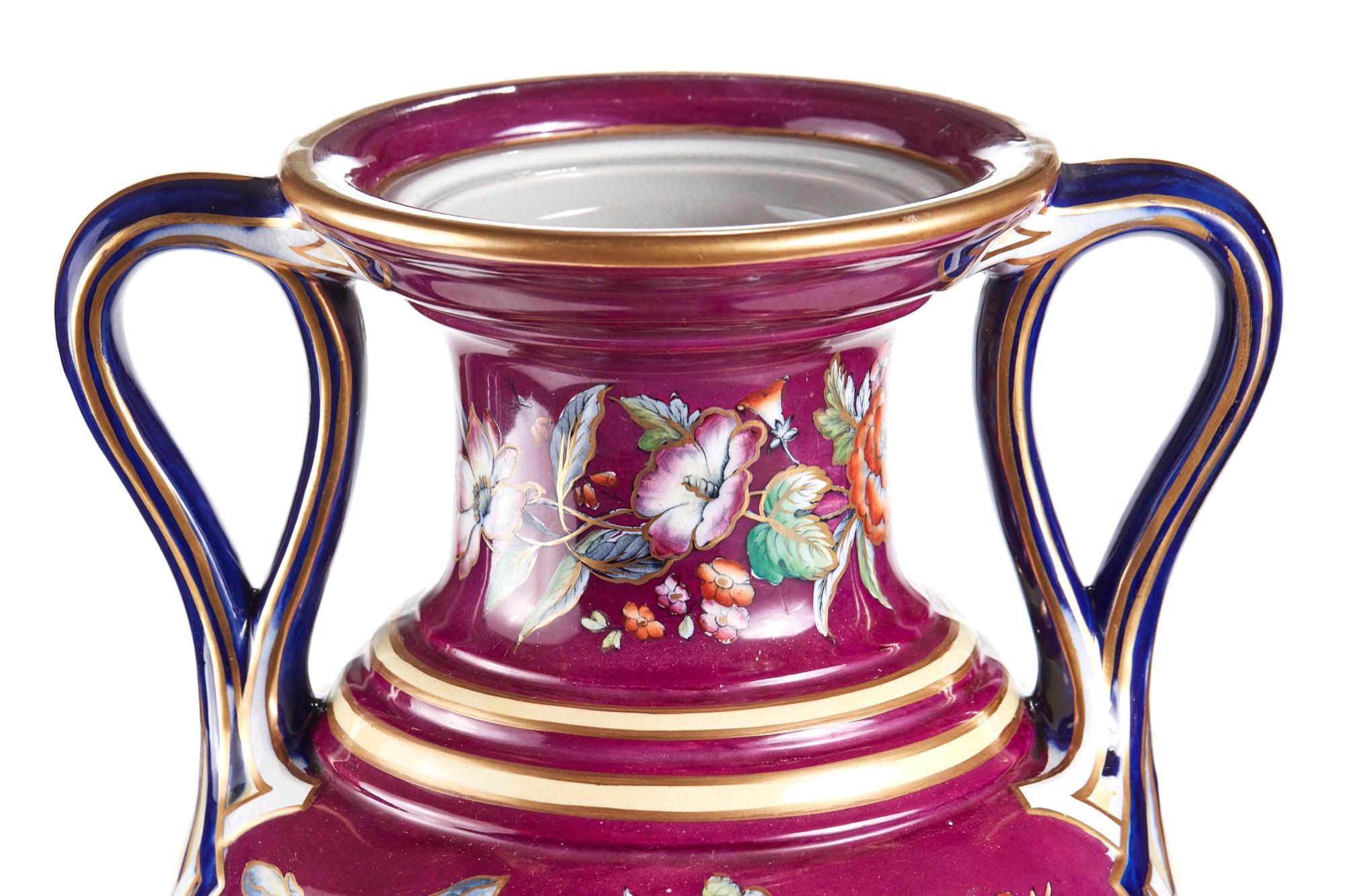 This is a large Staffordshire porcelaneous twin handled vase. The 57 cm high vase raised on pedestal shaft to a bulbous body and a trumpet shaped rim enclosed by two twin loop handles decorated with mauve ground and picked out with a spray of