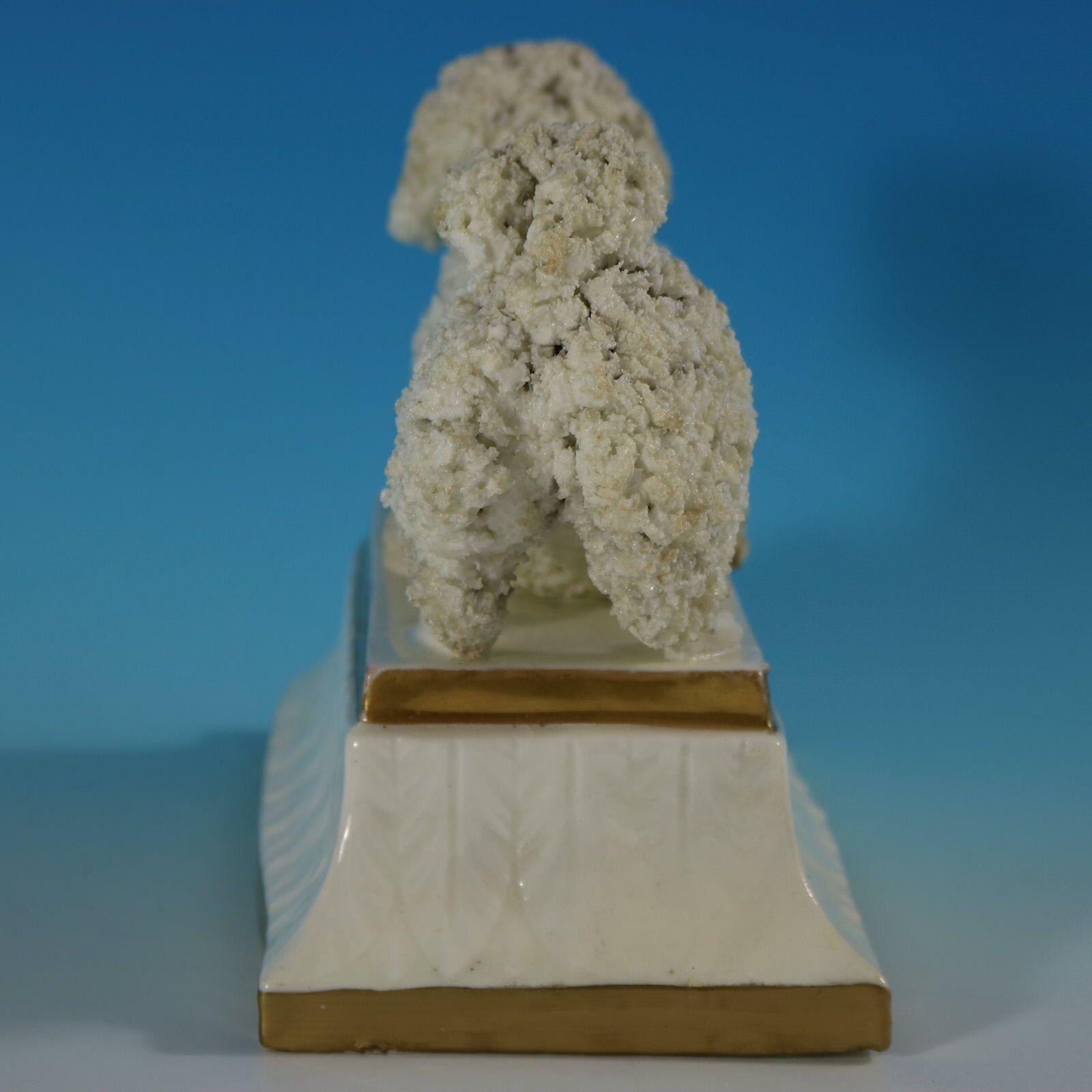 Staffordshire Pottery porcellaneous figure which features a poodle in a playful pose, crouched on a rectangular base. The base has leaf molding around the sides and has two dull gilt base lines.