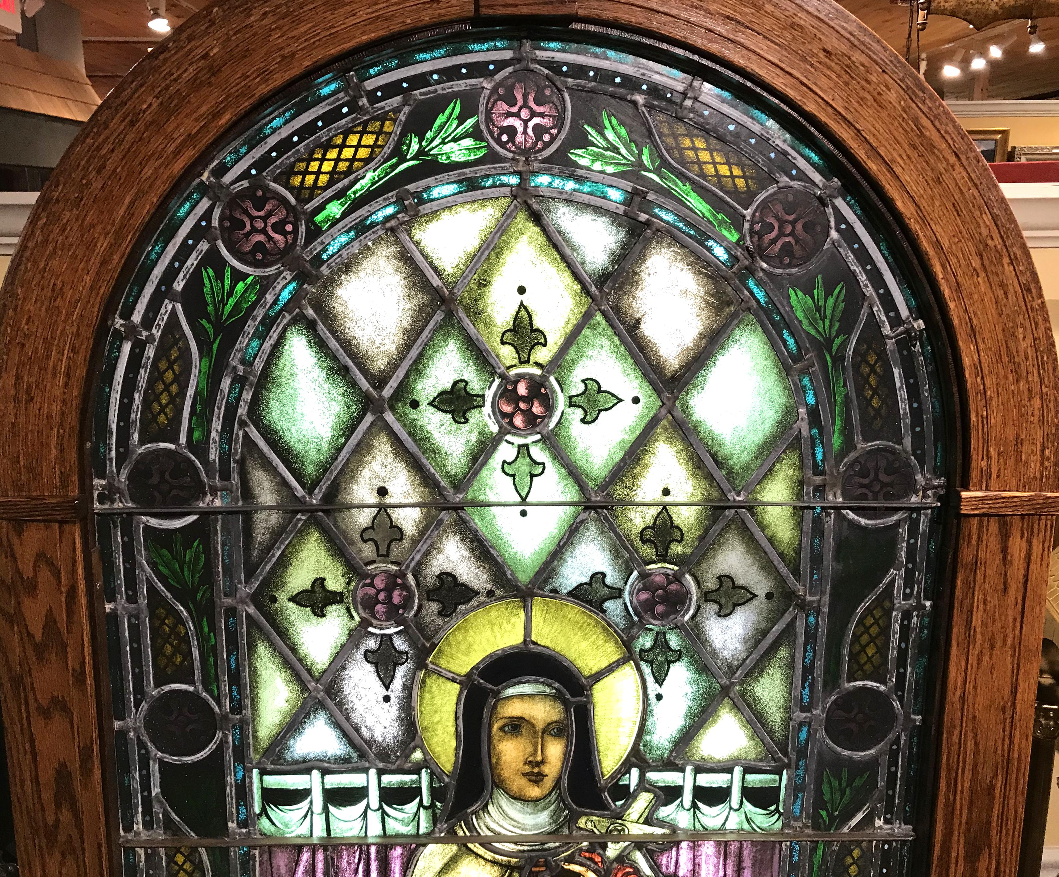 A splendid arched leaded stained glass window featuring Saint Thérèse de L’Enfant Jesus, commonly known as Saint Therese of the Child Jesus and the Holy Face, Saint Thérèse of Lisieux, or “The Little Flower”. She was born Marie Françoise-Therese