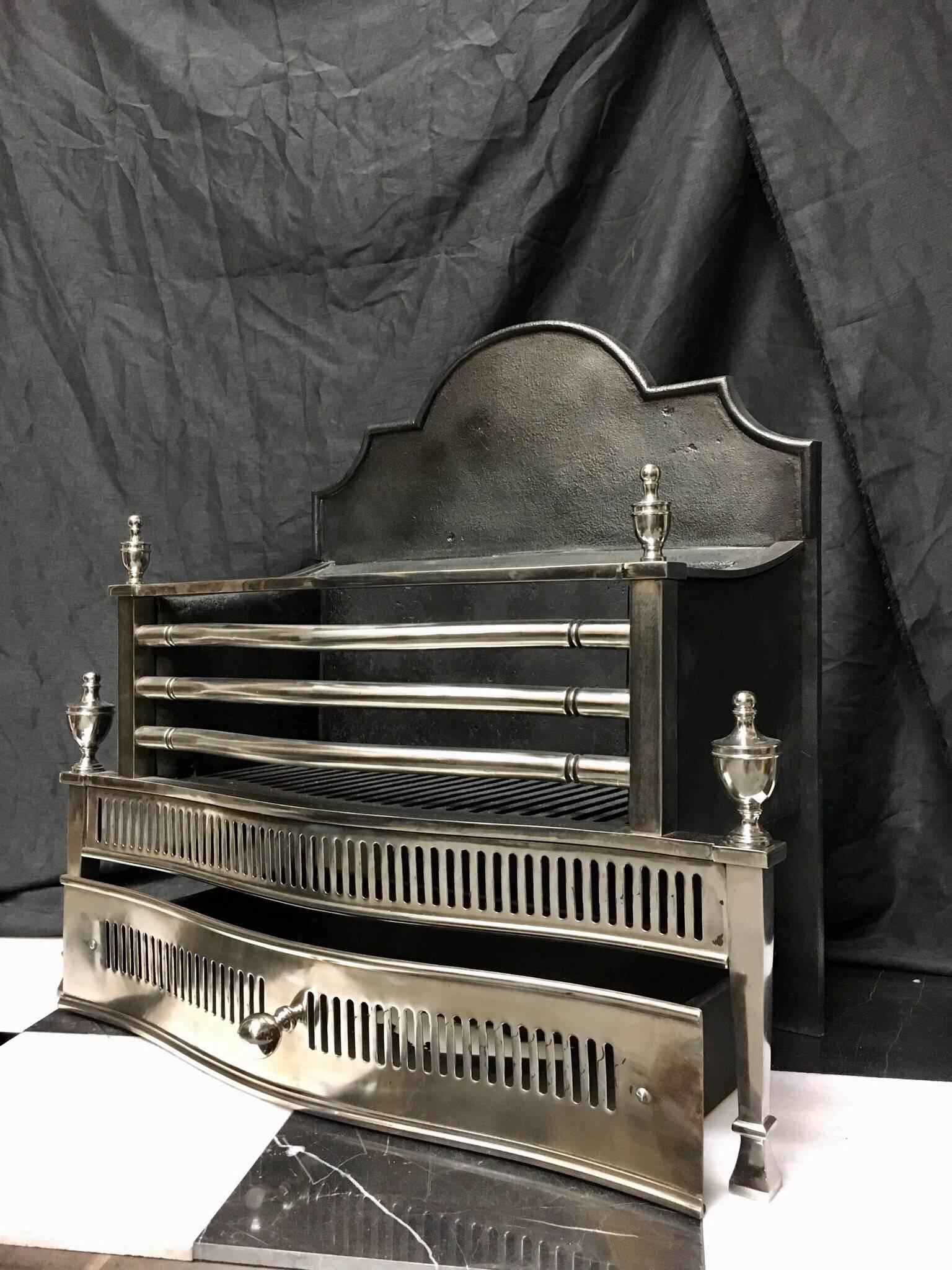 A large steel and cast iron four barred grate in the Georgian style with a fluted serpentine pierced apron. The grate is surmounted by a pair of polished finials with a further taller pair topping the tapered standards, all set beneath a tall shaped