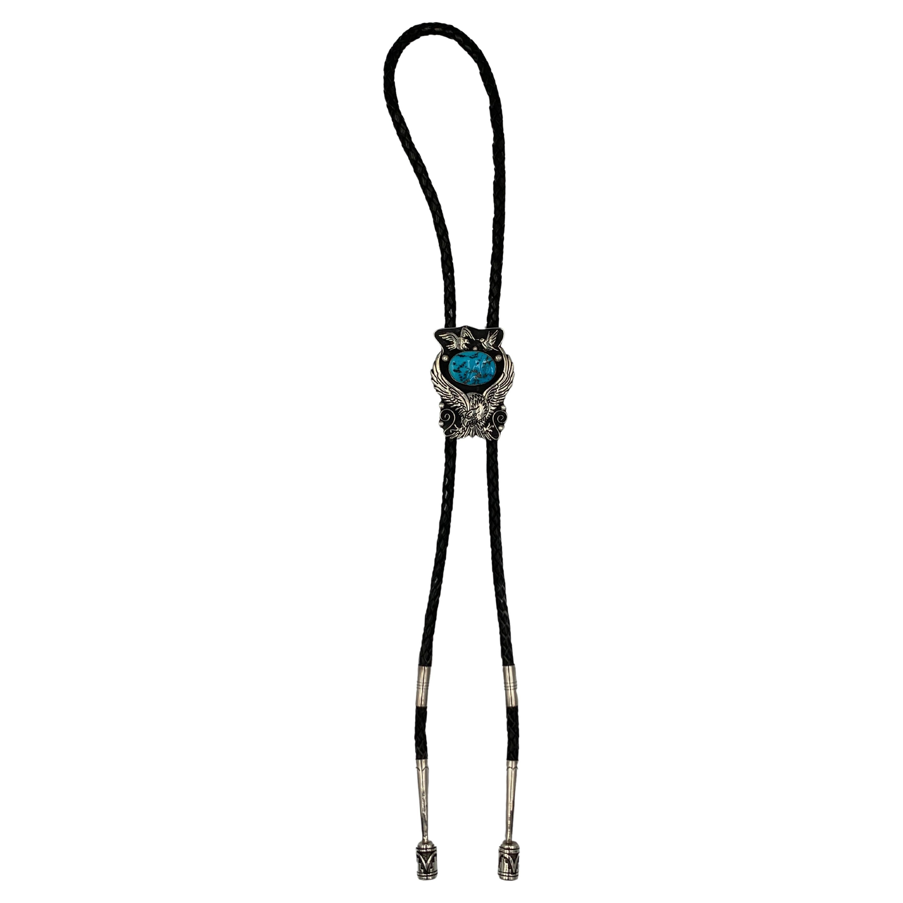 Sterling Silver Bolo Tie with Overlaid and Hand-Stamped Designs and set with Natural Candelaria Turquoise by Award Winning Navajo Silversmith, Tommy Singer (1940 - 2014). This bola tie features a 44” black leather cord, a custom backing, and
