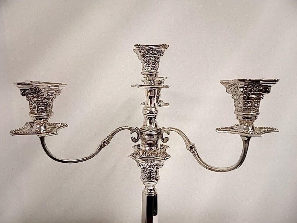 This is a stunning George V sterling silver four light candelabra. It has campana shaped sconces and three S-scroll branches above knopped and waisted stems of square form with canted corners above stepped loaded bases, convertible to a candlestick.