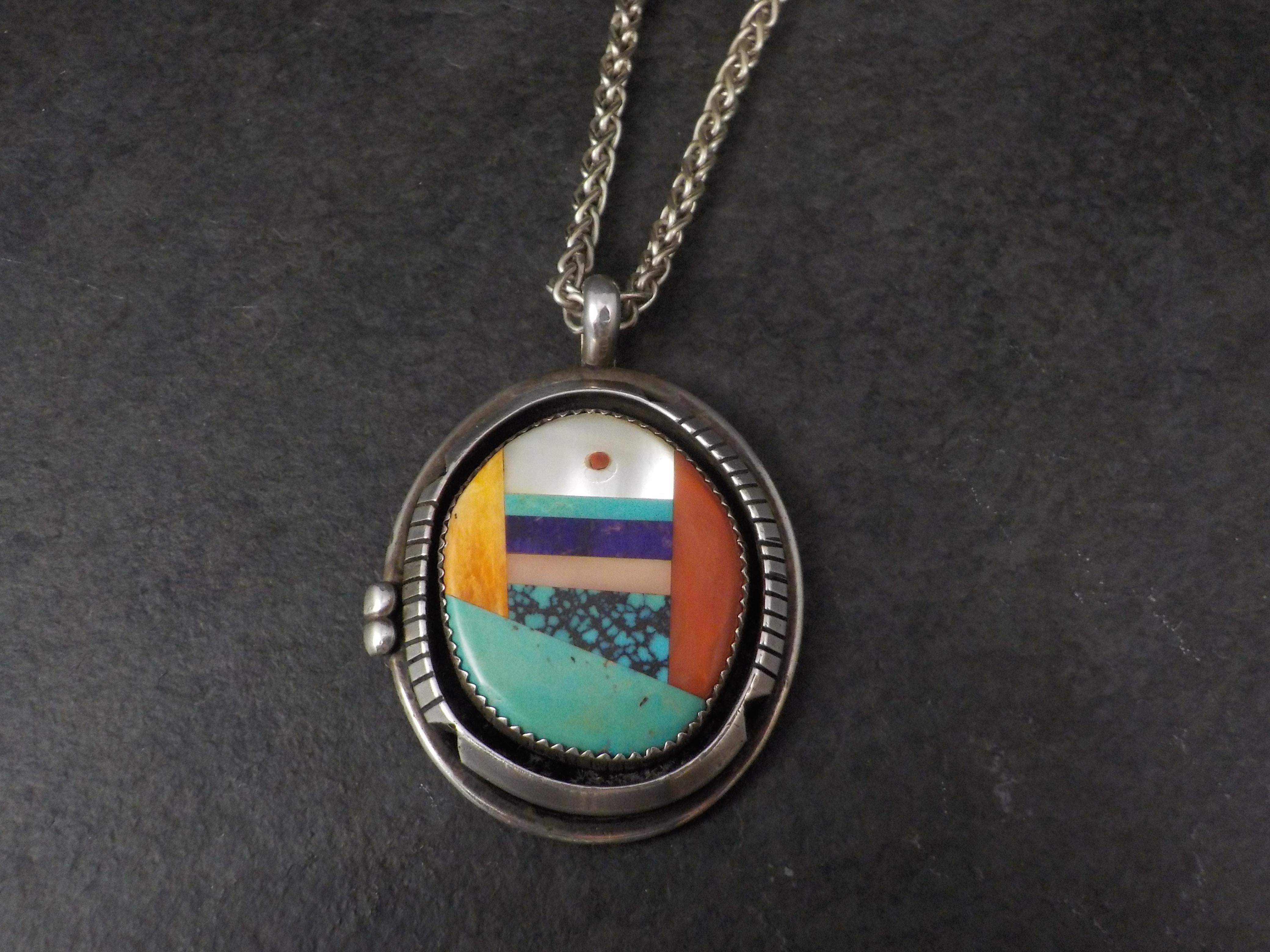 This beautiful, vintage Native American pendant is sterling silver.
It features inlay in pink and white mother of pearl, spiny oyster, coral, turquoise and sugilite.

The pendant measures 1 1/2 by 2 inches.
The 3mm Italian made wheat chain is