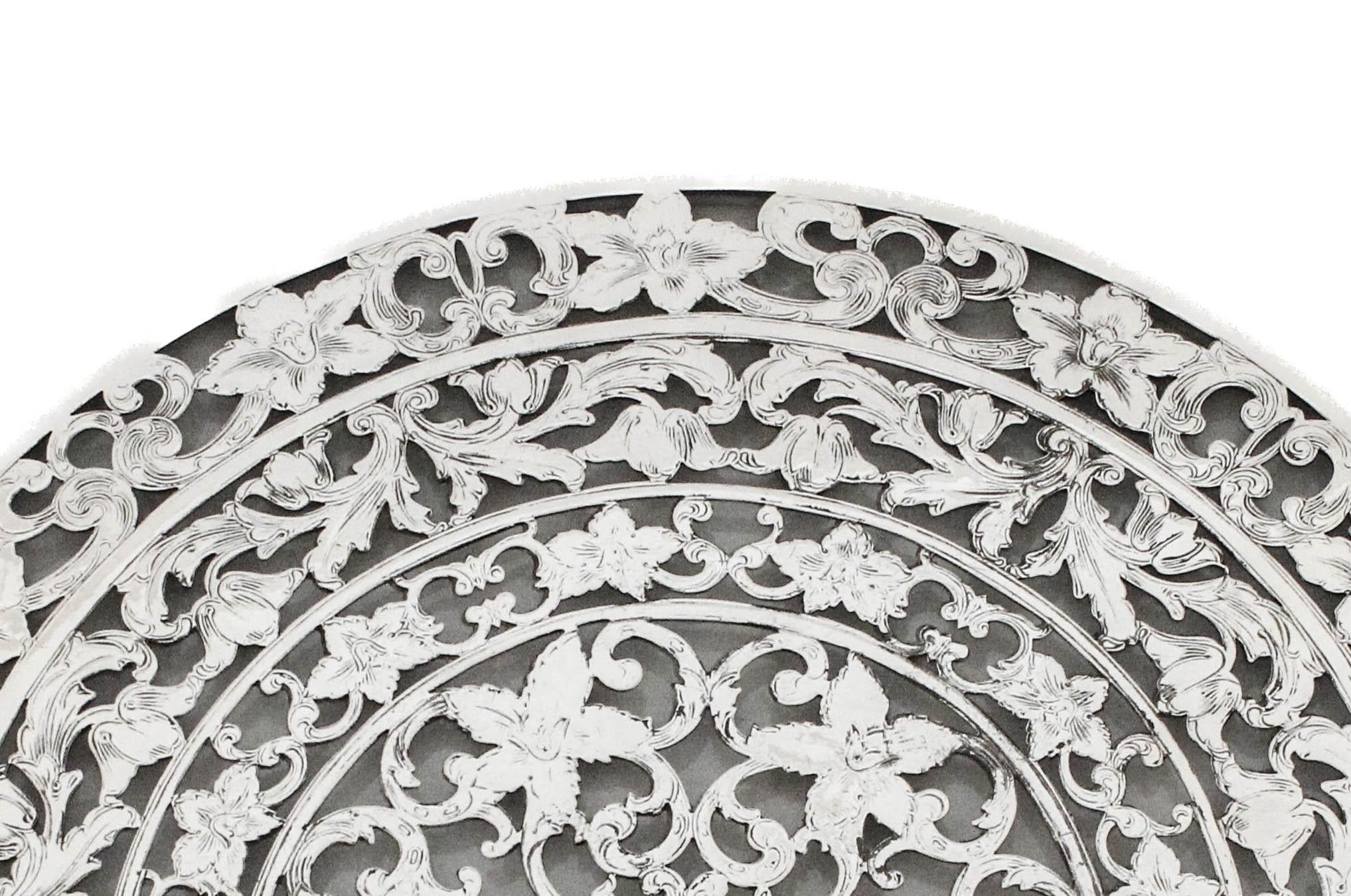 Ce dessous-de-plat exquis en argent sterling date du début du XXe siècle et reste en parfait état. La pièce présente un motif élaboré et finement détaillé, probablement appliqué sur du verre, illustrant l'esthétique ornementale en vogue à l'époque