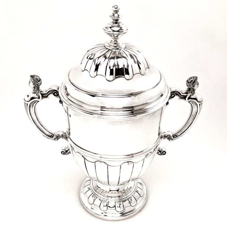 An impressive solid Silver Trophy with a substantial domed lid. The Trophy has two scroll handles topped with detailed classical heads. The cup and cover have wide fluting on the base, foot and lid, leaving a wide flat band for engraving if desired.